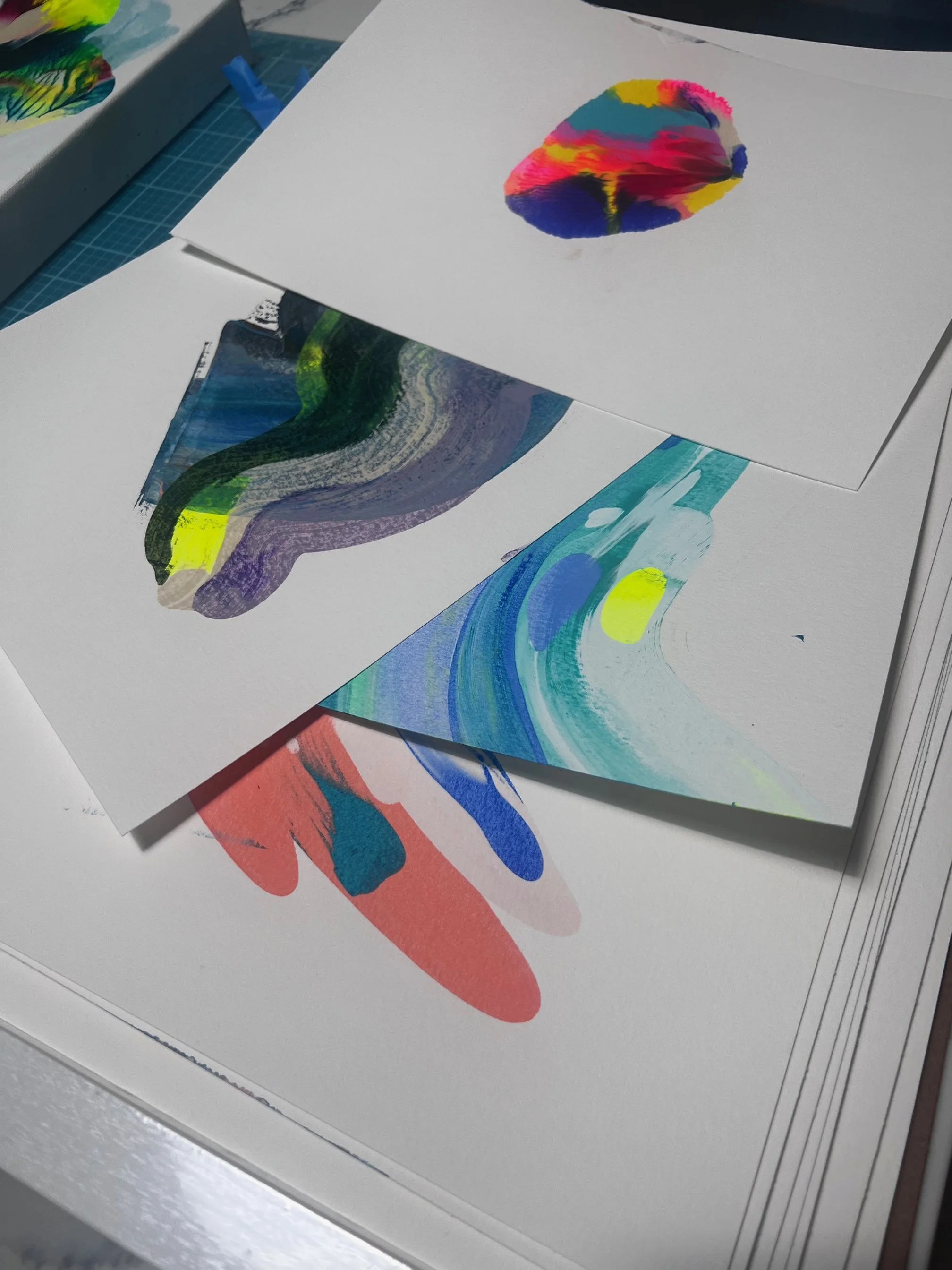 Several sheets of paper with abstract colorful paintings on a desk.