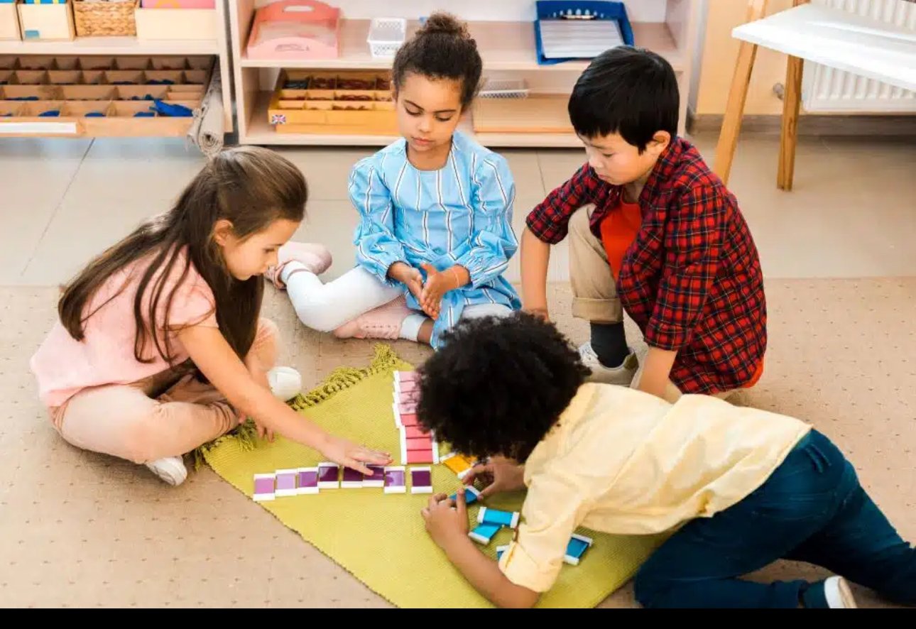 Four children playing a tile matching game on a yellow rug in a classroom.