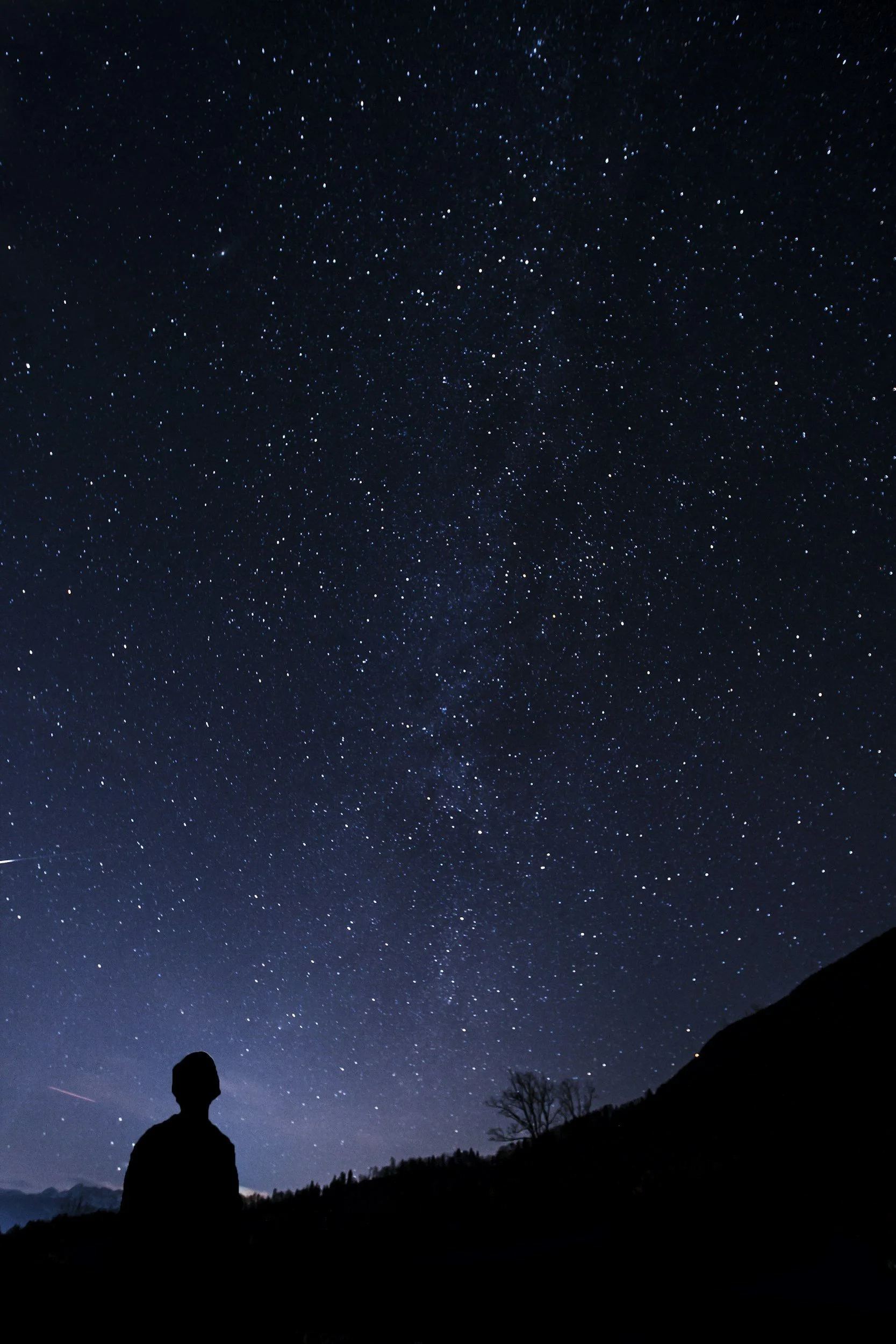 Silhouette of a person standing outdoors at night, looking at a star-filled sky and the Milky Way galaxy.