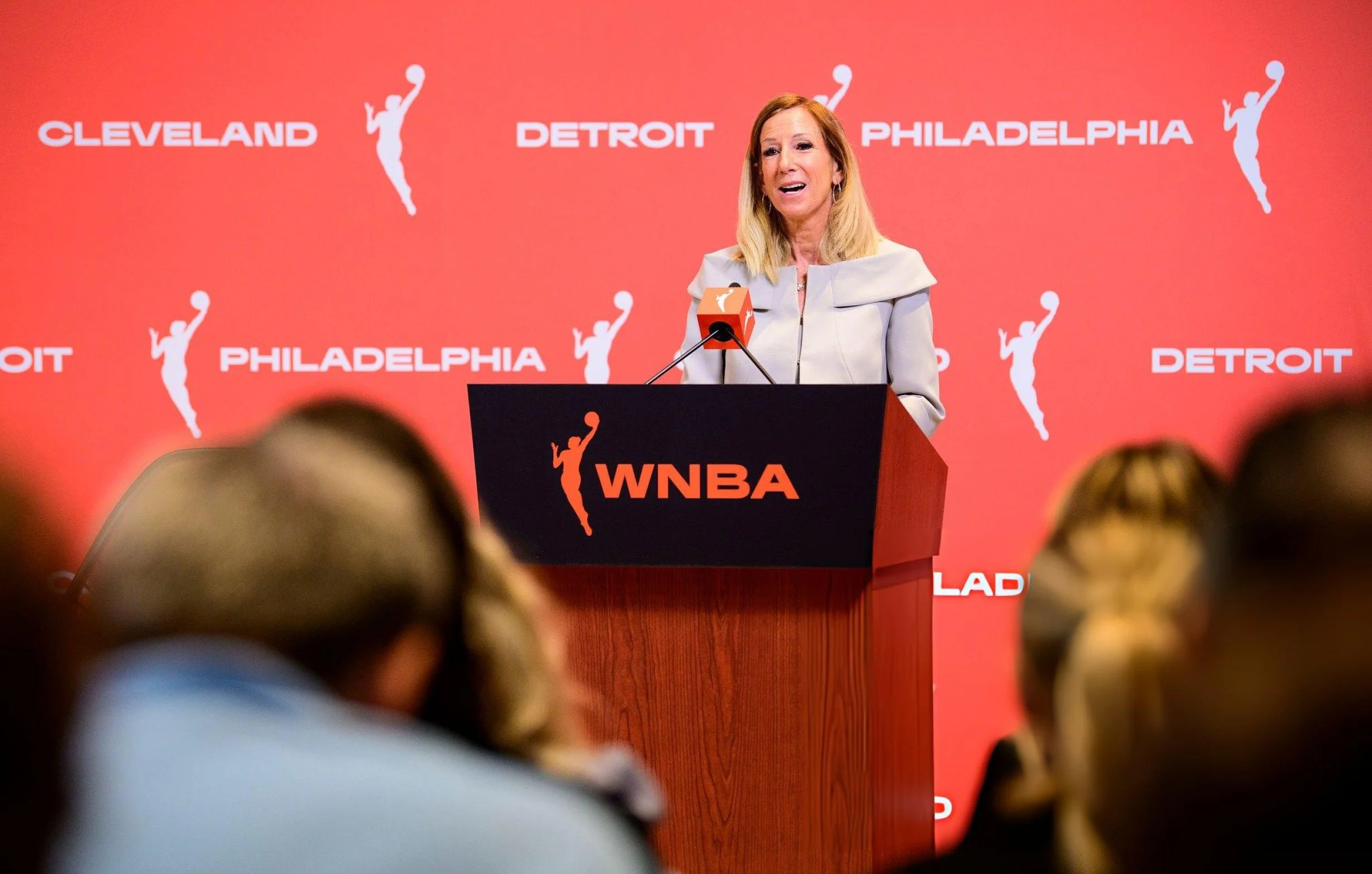 Four people sitting on stools during a panel discussion at an event with a red backdrop featuring the words 'Detroit,' 'Philadelphia,' 'Cleveland,' and a basketball player silhouette.