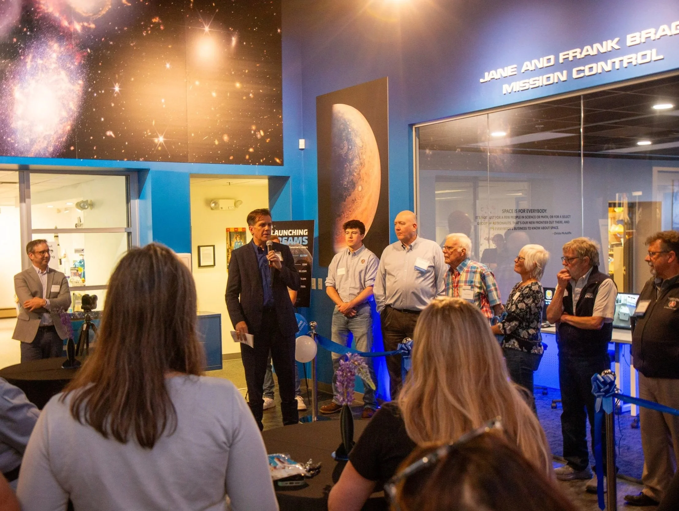 Adult with a microphone speaking to a crowd of adults in the lobby of Challenger Maine