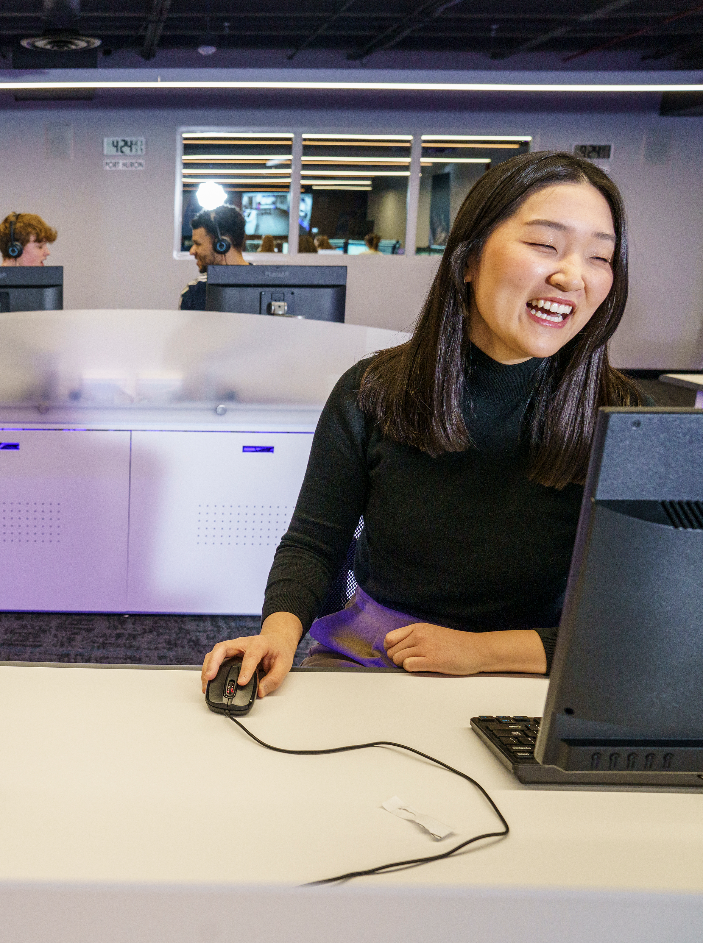 A teenage student in a black turtleneck smiling and working at a NASA simulator station in the Challenger Center,