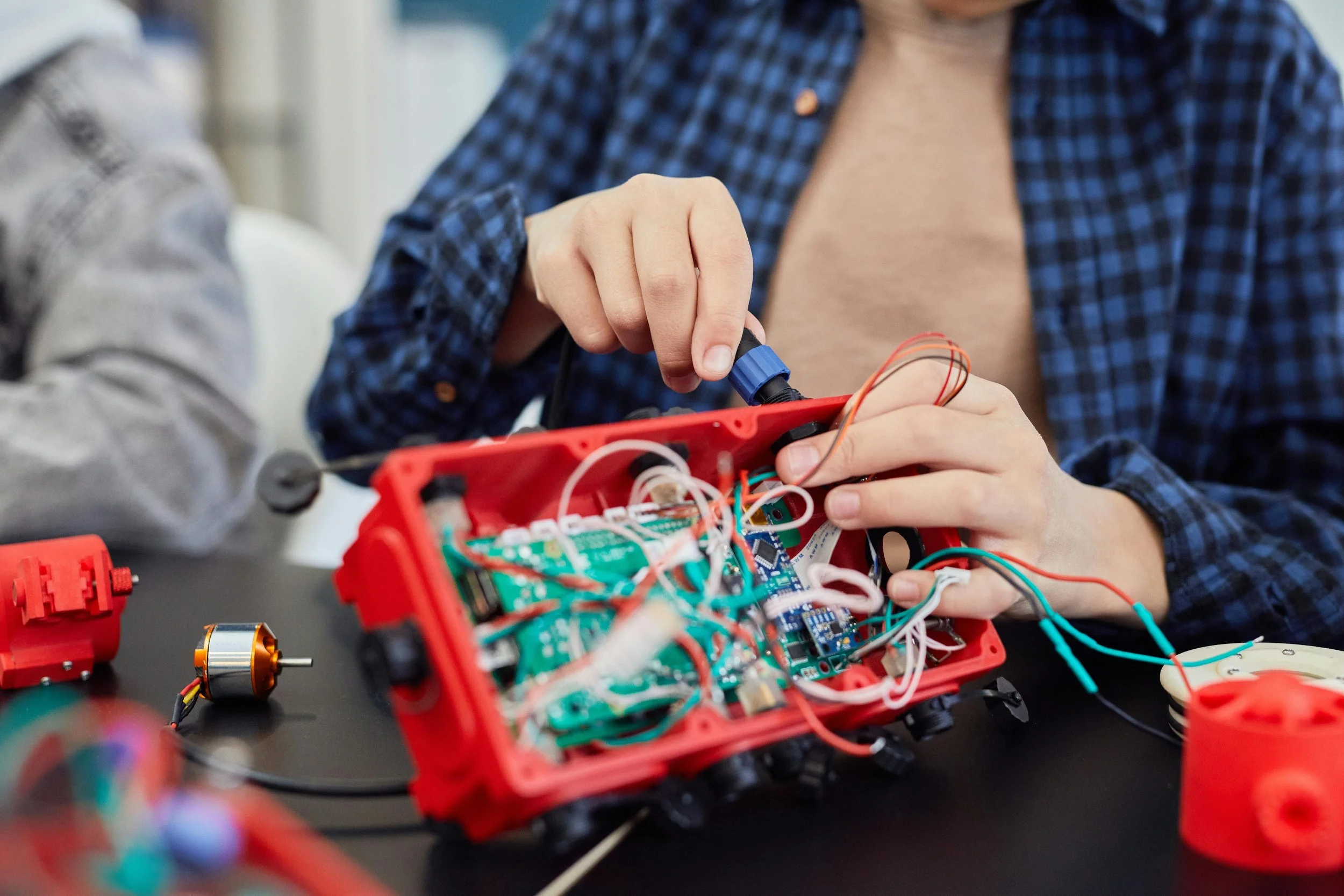 Student working on an electronic circuit inside a red enclosure with wires and components, on a black table.