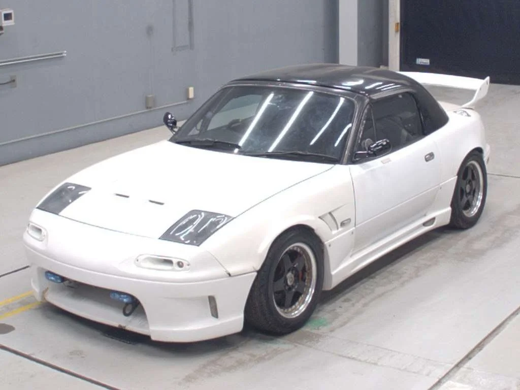 White sports car with black roof and racing spoiler parked indoors.