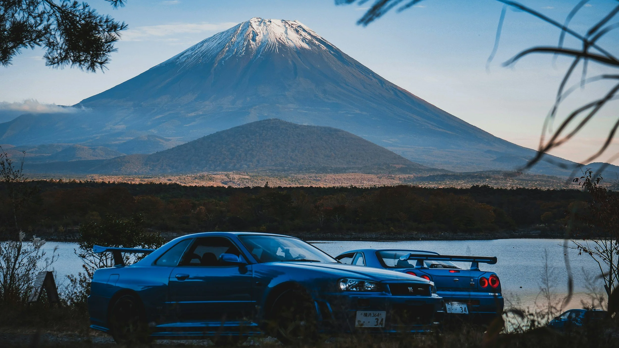 large mountain with two blye nissan skyline gtr's with a lake in the background