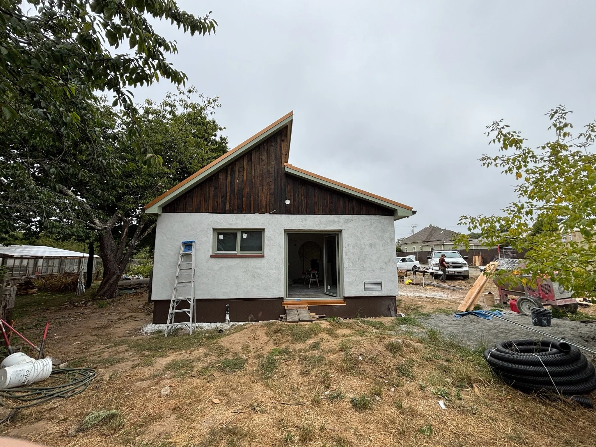 Under construction house with a sloped roof, unfinished driveway, and construction equipment on a cloudy day.