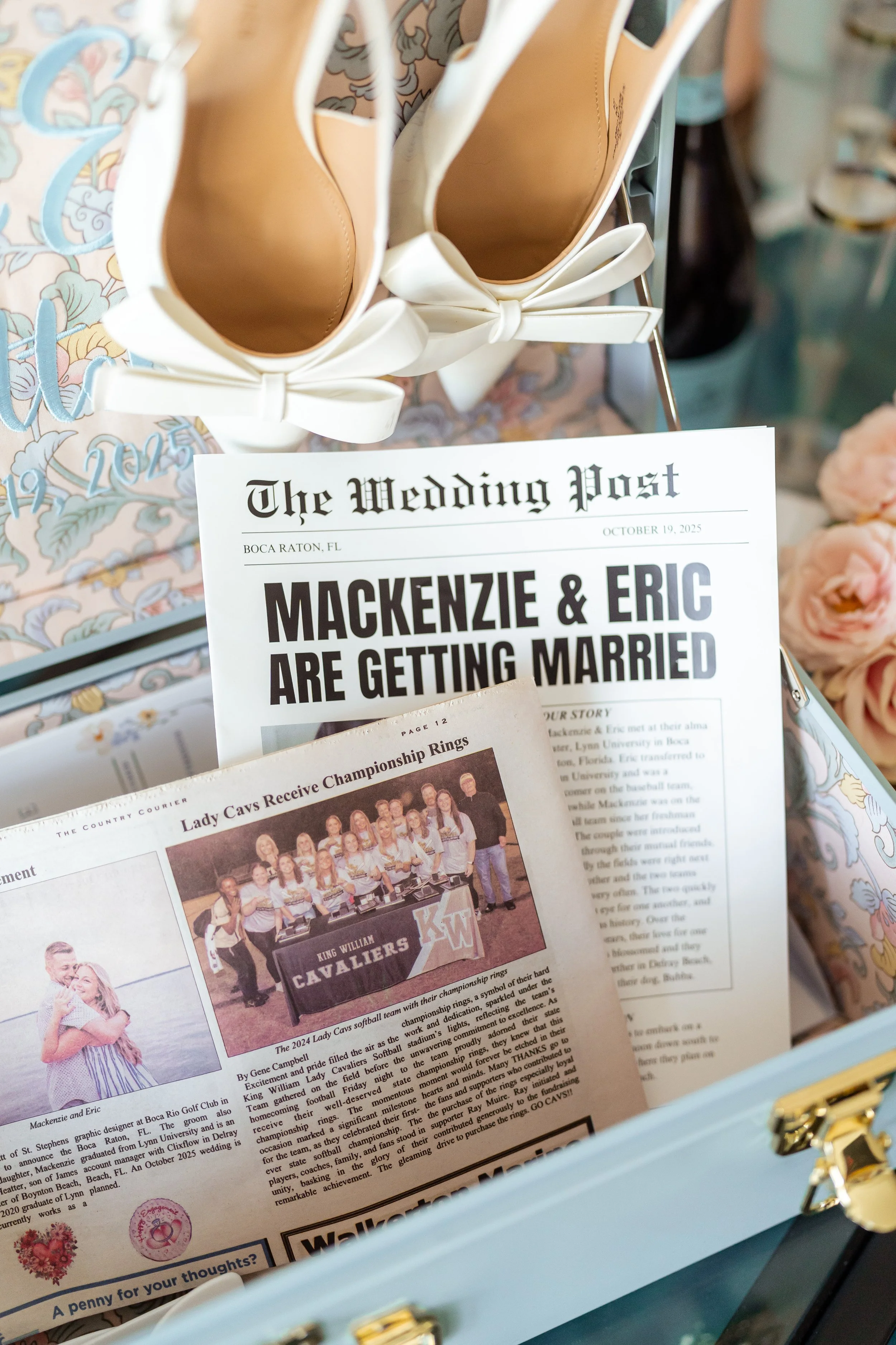 A close-up photo of a light blue wedding box with gold-colored details, containing newspapers and congratulatory cards, with white shoes that have bows on top. There is also a visible wedding invitation from 'The Wedding Post' with headlines about Ma