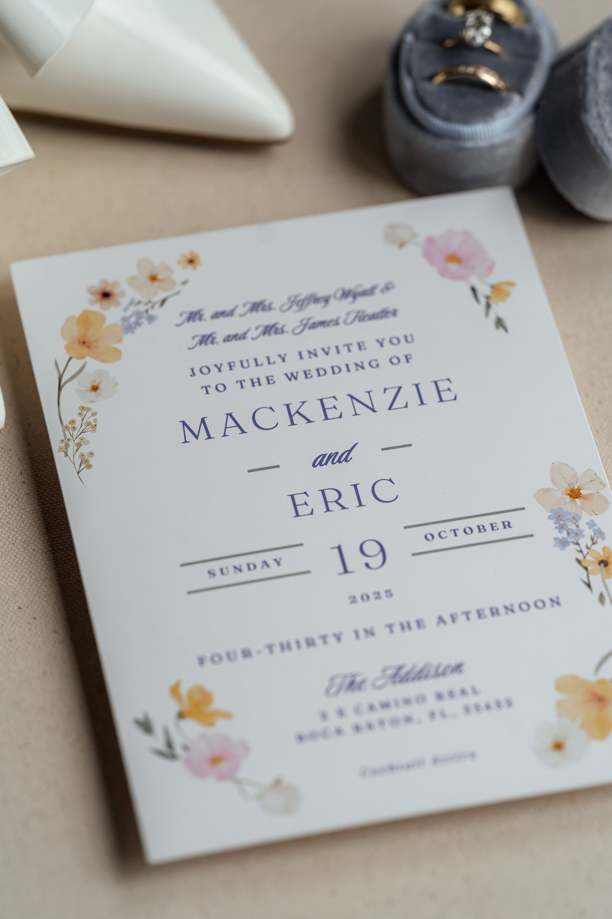 Wedding invitation with floral design, featuring the names Mackenzie and Eric, an October date, and details for a Sunday wedding in the afternoon.