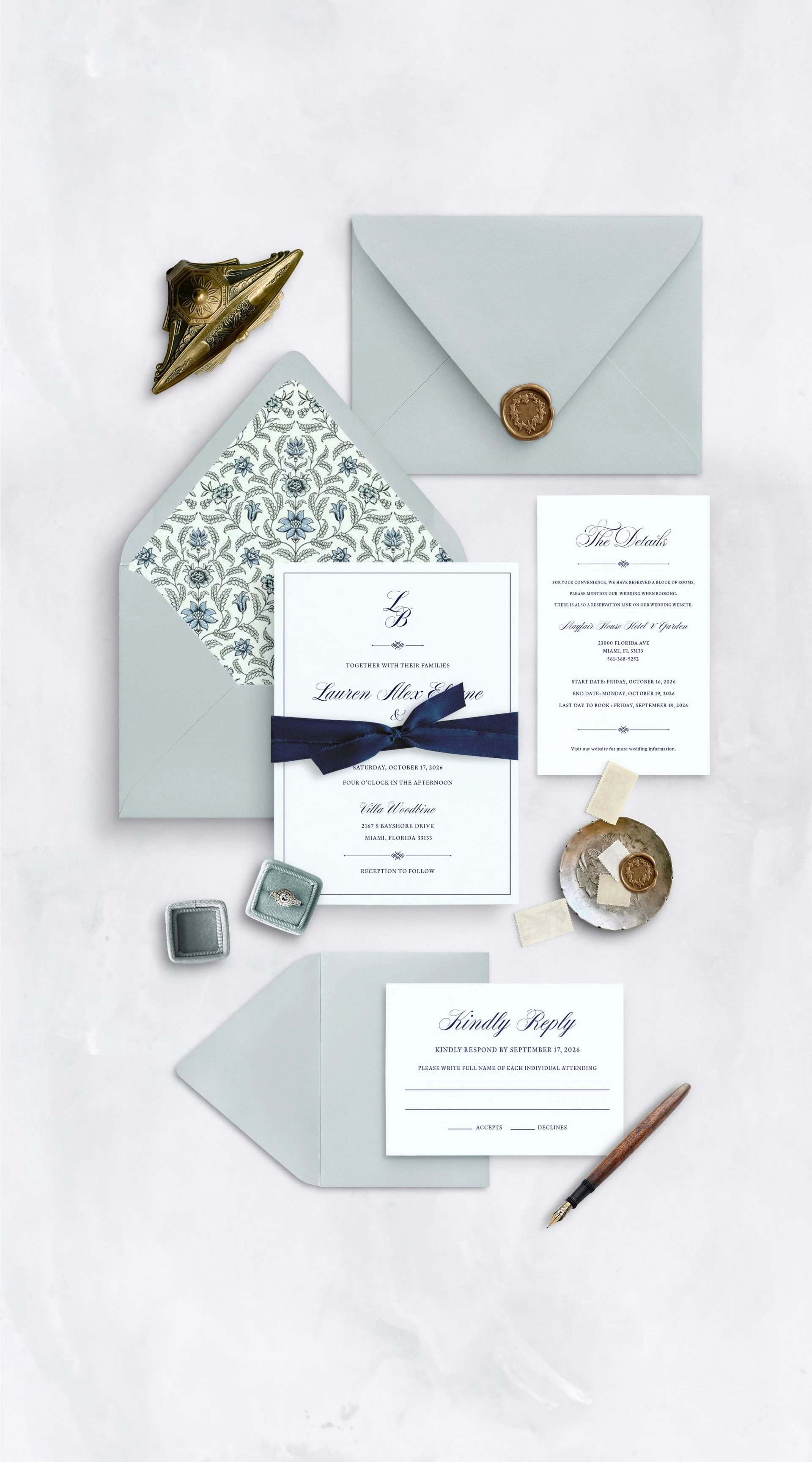 Wedding invitation suite on a white background, including an envelope with a wax seal, a patterned lining, RSVP and details cards, a small box with a ring, and vintage sealing wax tools.