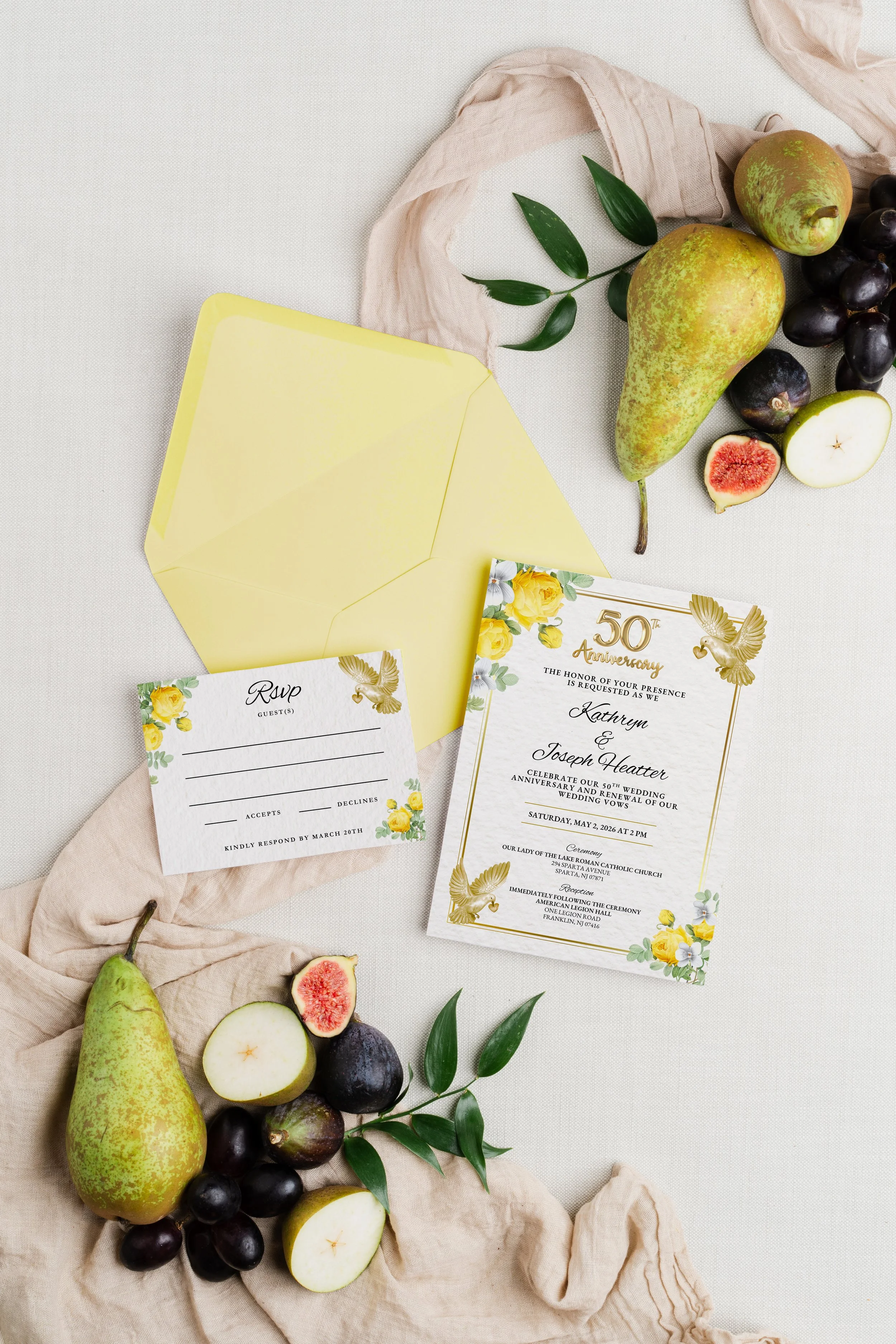 Wedding invitation card, RSVP card, yellow envelope, green pears, black grapes, figs, green leaves on beige fabric background.