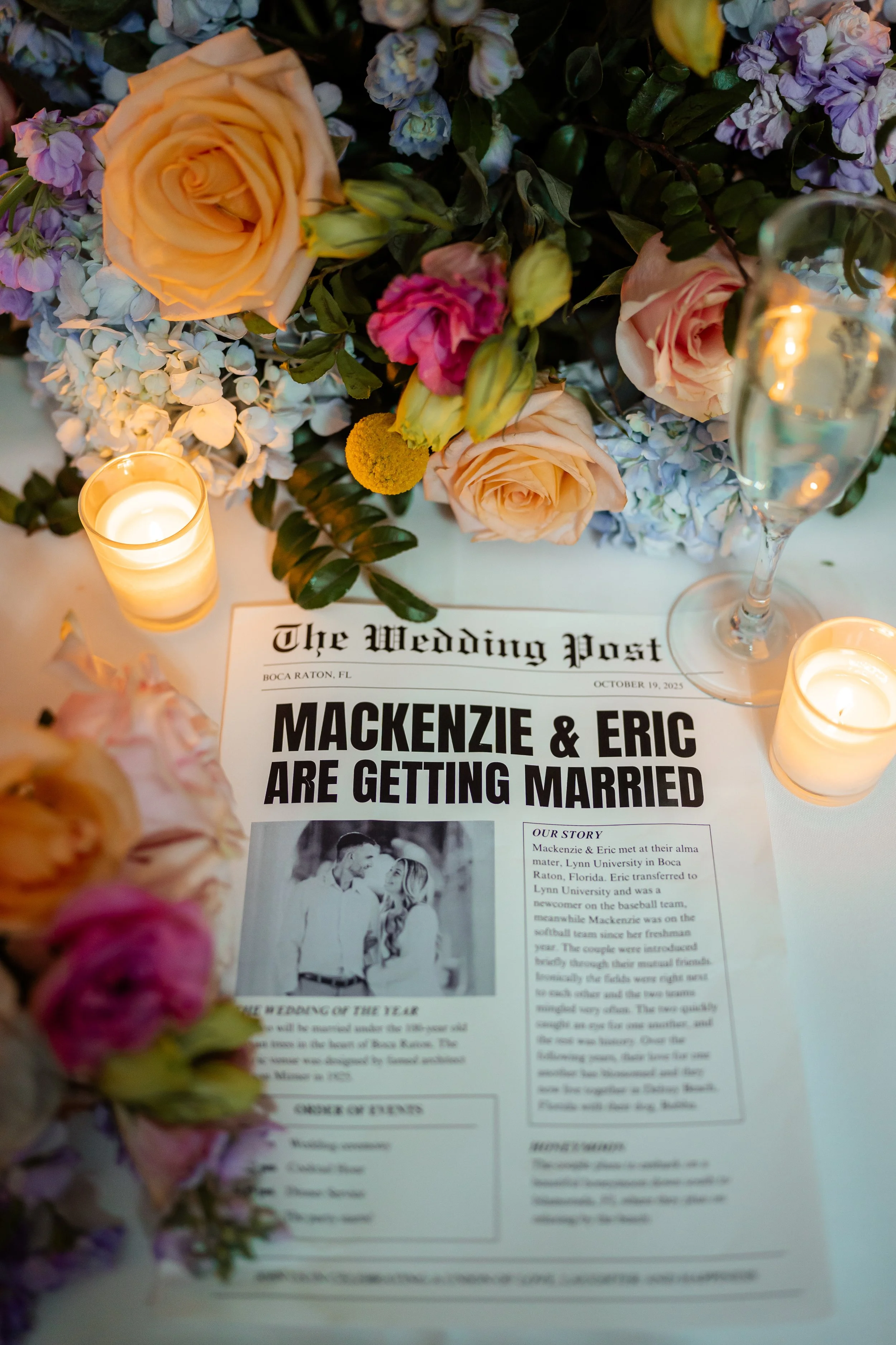 Wedding reception table with floral centerpiece, candles, a champagne glass, and a wedding announcement newspaper for Mackenzie and Eric's wedding.