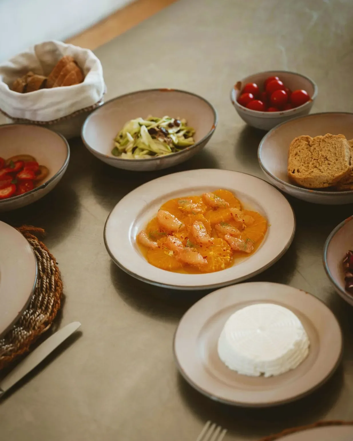 A variety of dishes on a dining table, including shrimp in sauce, cherry tomatoes, sliced bread, cheese, and assorted vegetables.