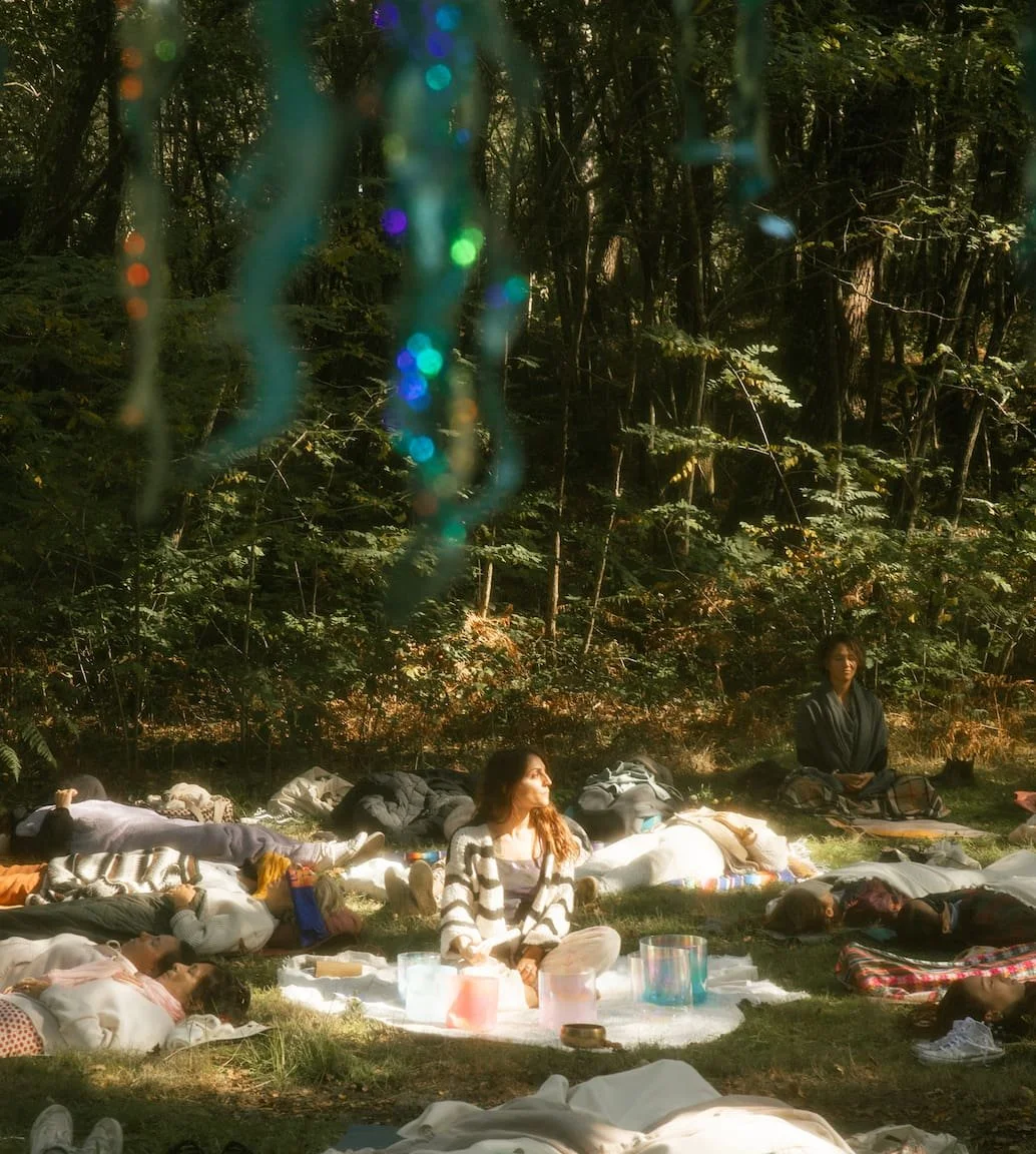 Laura, praticienne en bains sonores, guidant un bain sonore géant en forêt lors d’un festival, sous des lumières suspendues colorées.