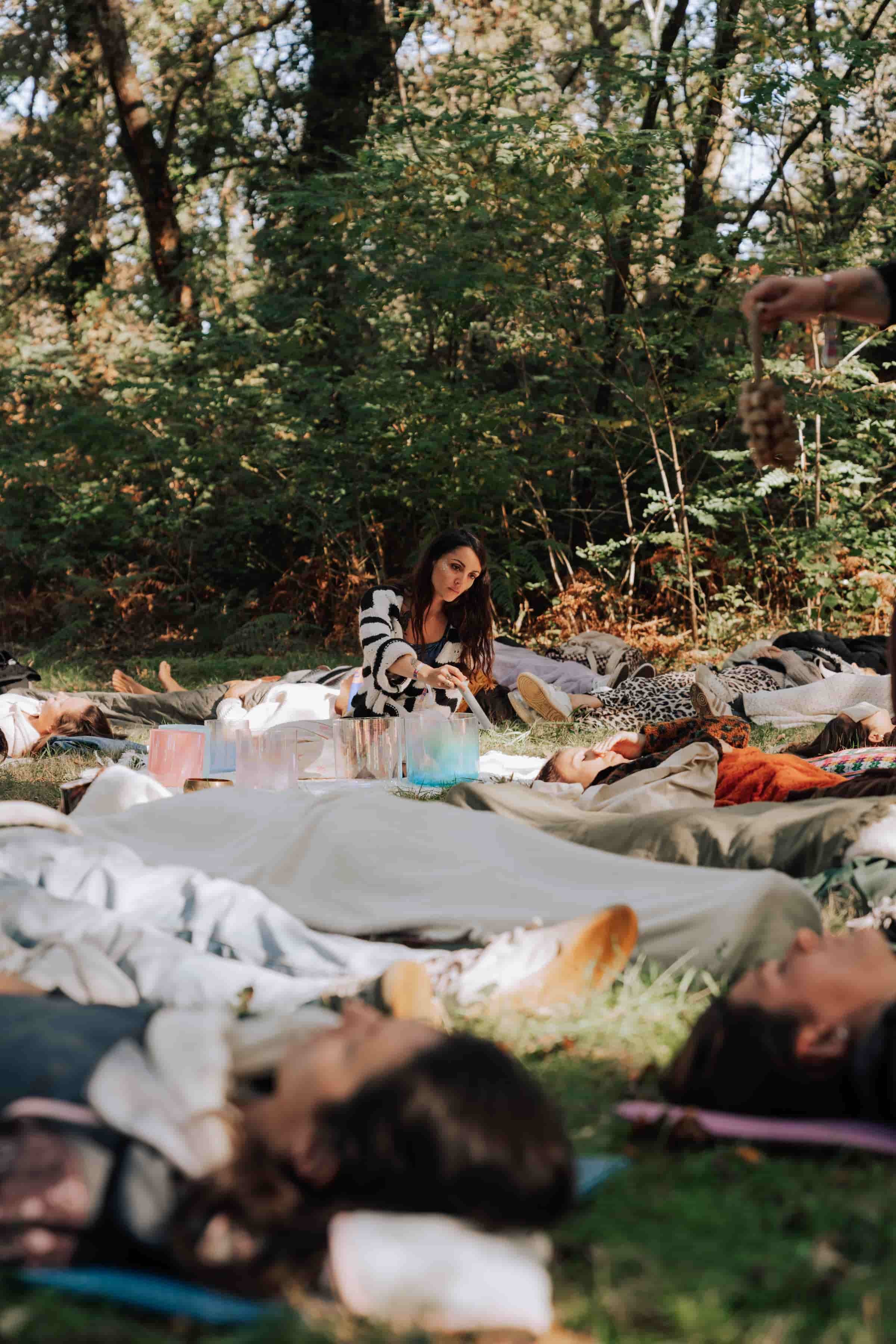 Laura, praticienne en bains sonores, guidant un bain sonore géant en forêt lors d’un festival, sous des lumières suspendues colorées.