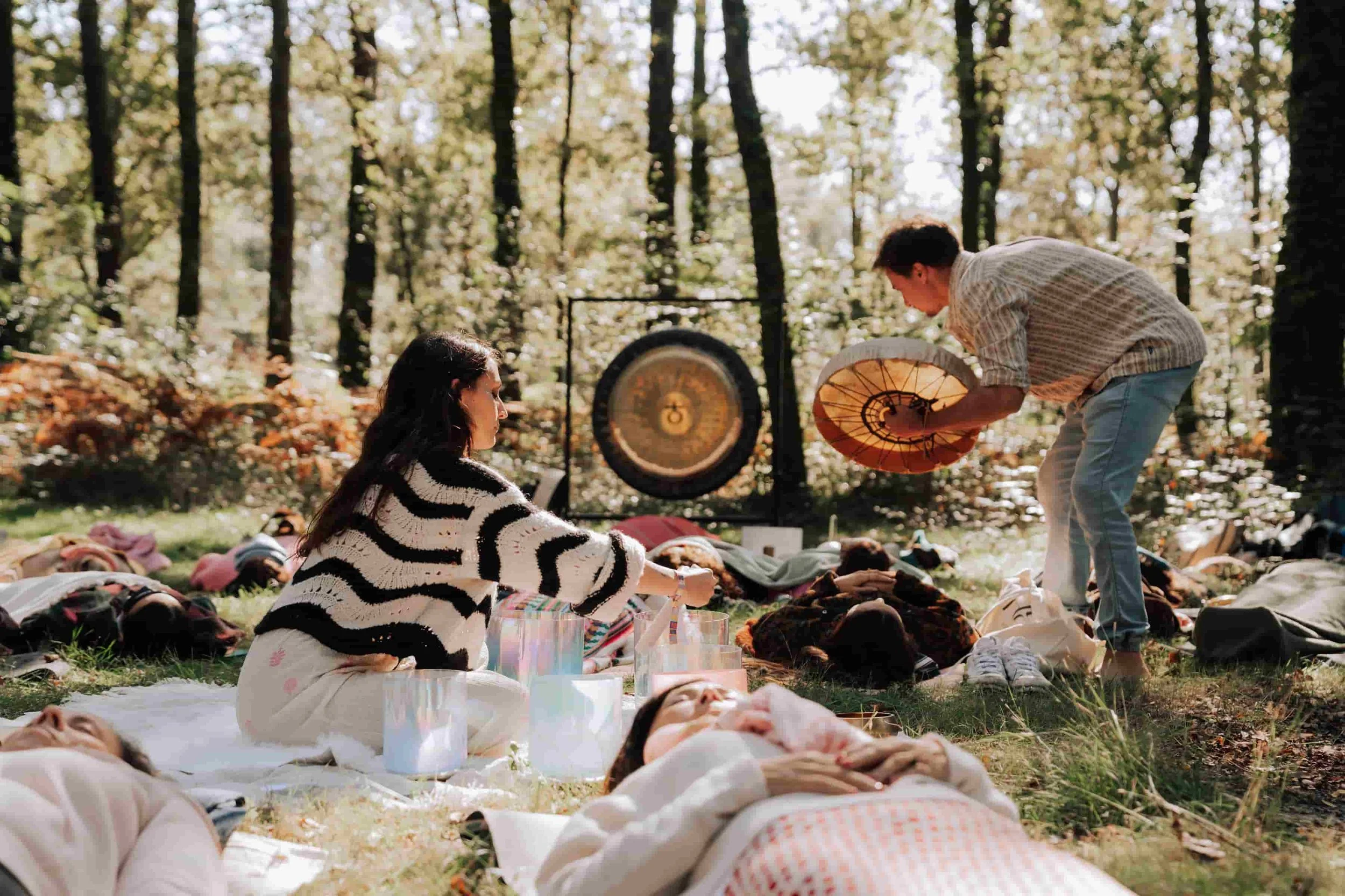 Laura, praticienne en bains sonores, guidant un bain sonore géant en forêt lors d’un festival, sous des lumières suspendues colorées.