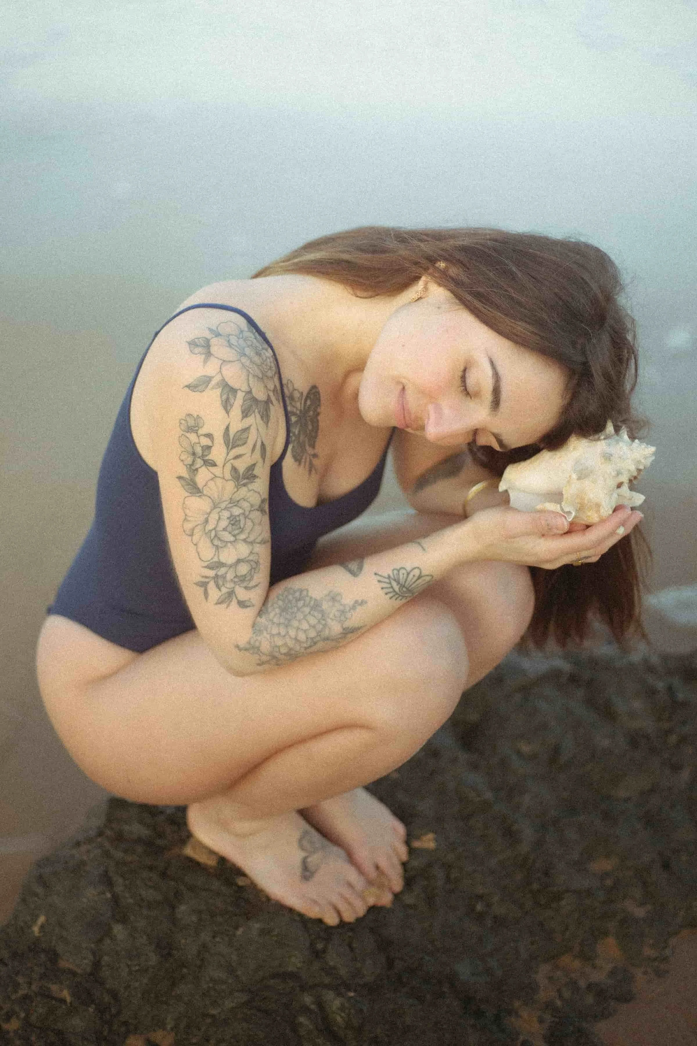 Laura, créatrice de bains sonores, conceptrice de sites et fleuriste freelance, au bord de l’océan tenant un coquillage.