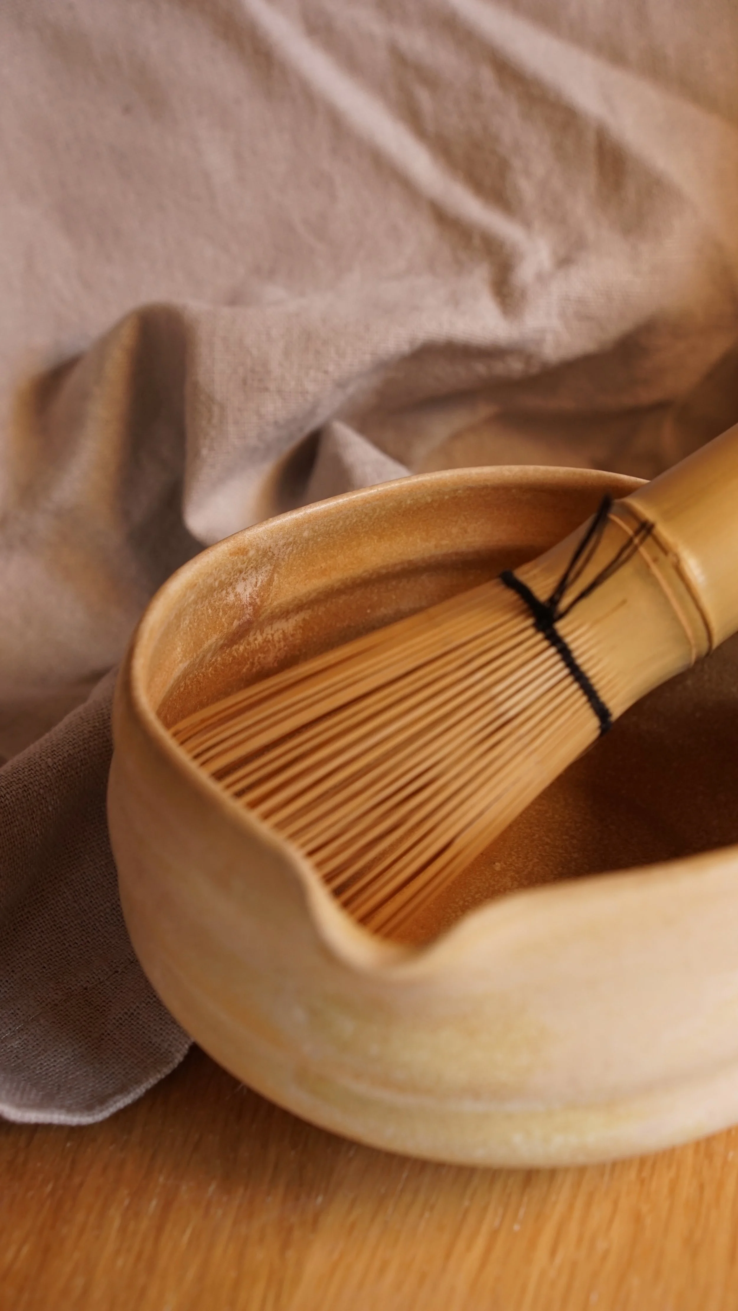 In einer organisch geformten sandfarbenen Matchaschale in der Glasur Düne liegt ein Chasen Matchabesen.