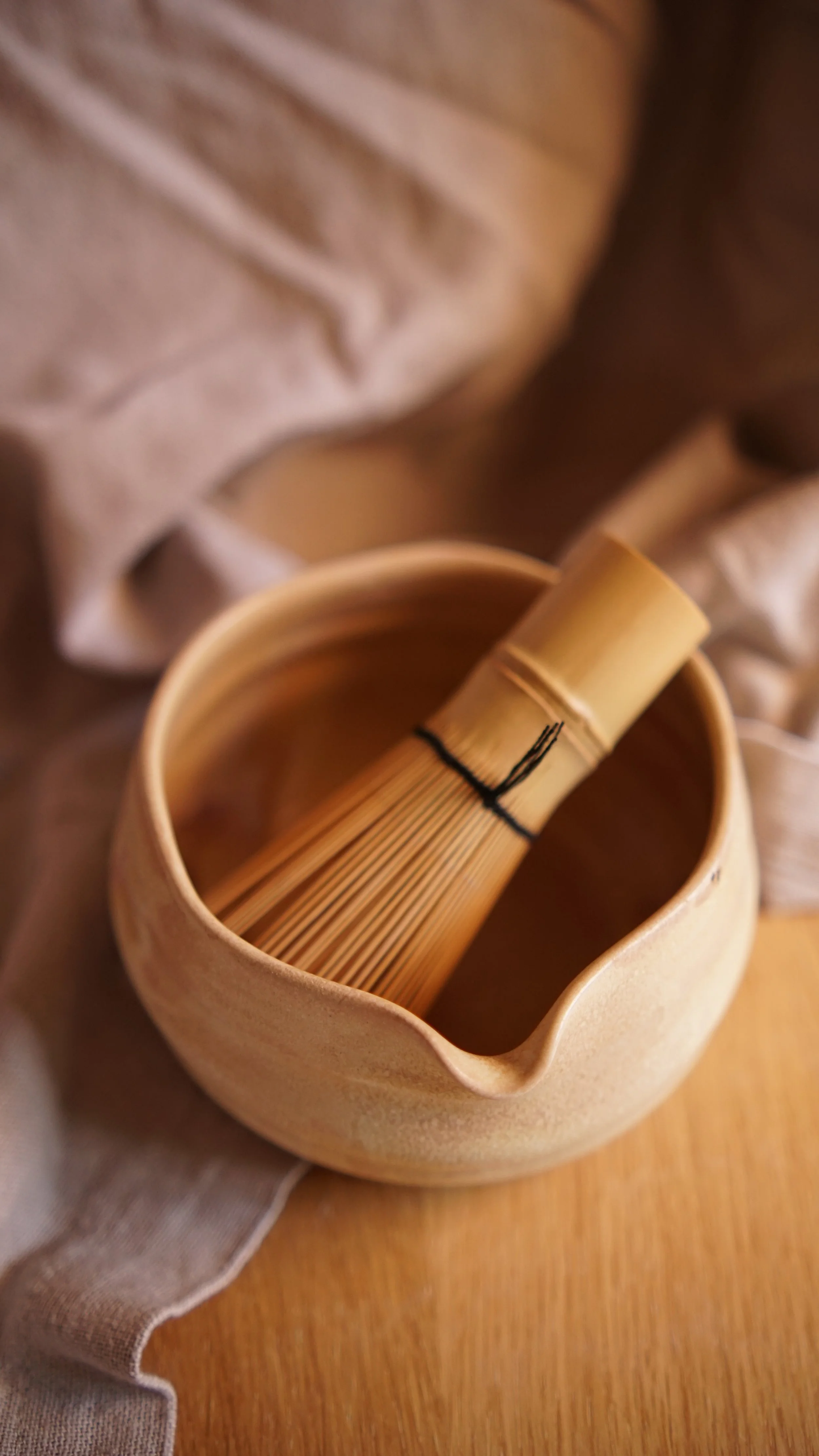 Ein Matchabesen liegt in einer sandfarbenen Matchaschale.