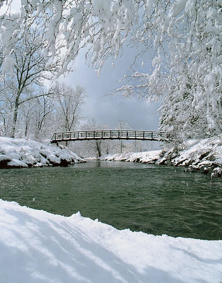 Stowe recreation path in winter with snow-covered trees and footbridge over river in Vermont