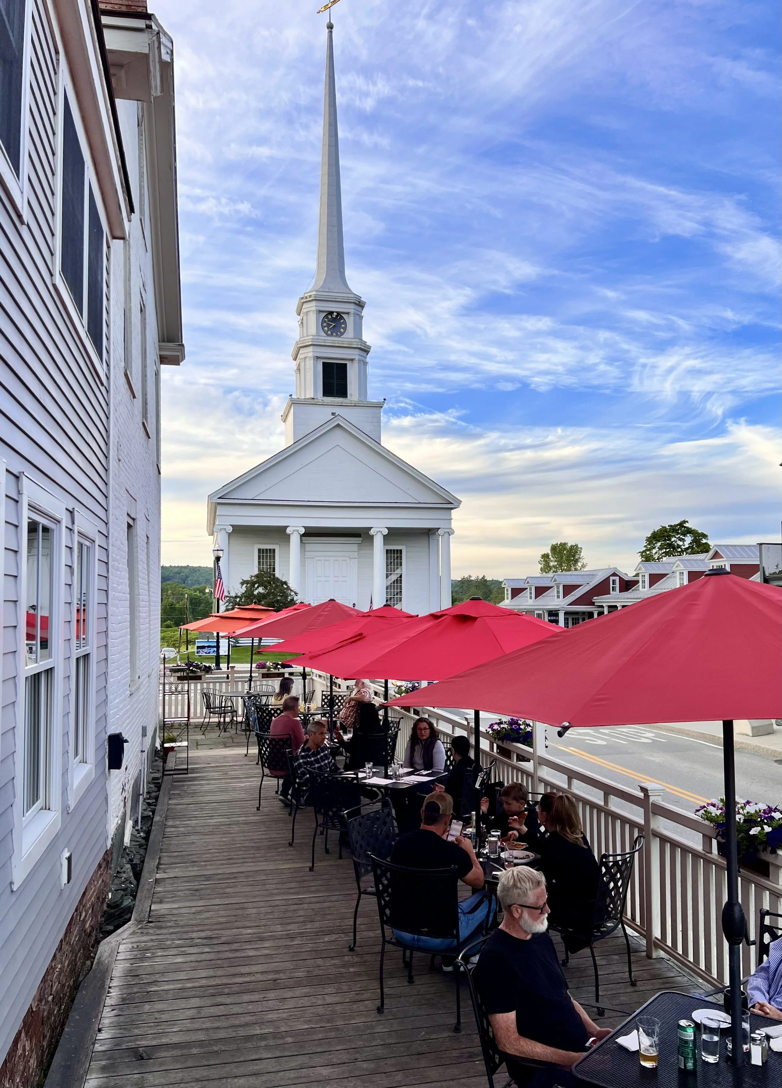Outdoor dining patio at Butler's Pantry in Stowe Vermont with red umbrellas and views of Stowe Community Church