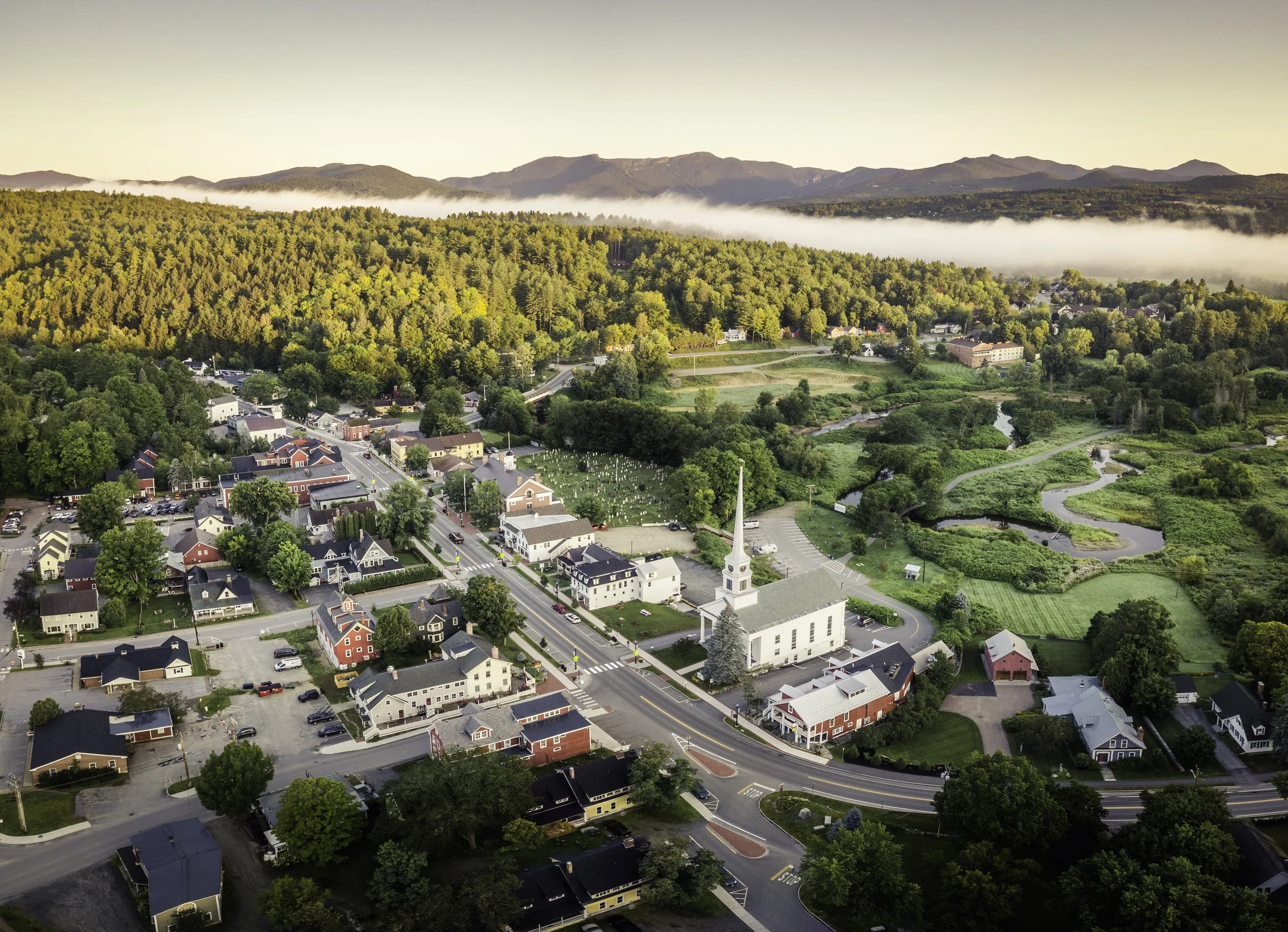 Aerial view of Stowe Village Vermont with white church steeple, mountain backdrop and surrounding countryside