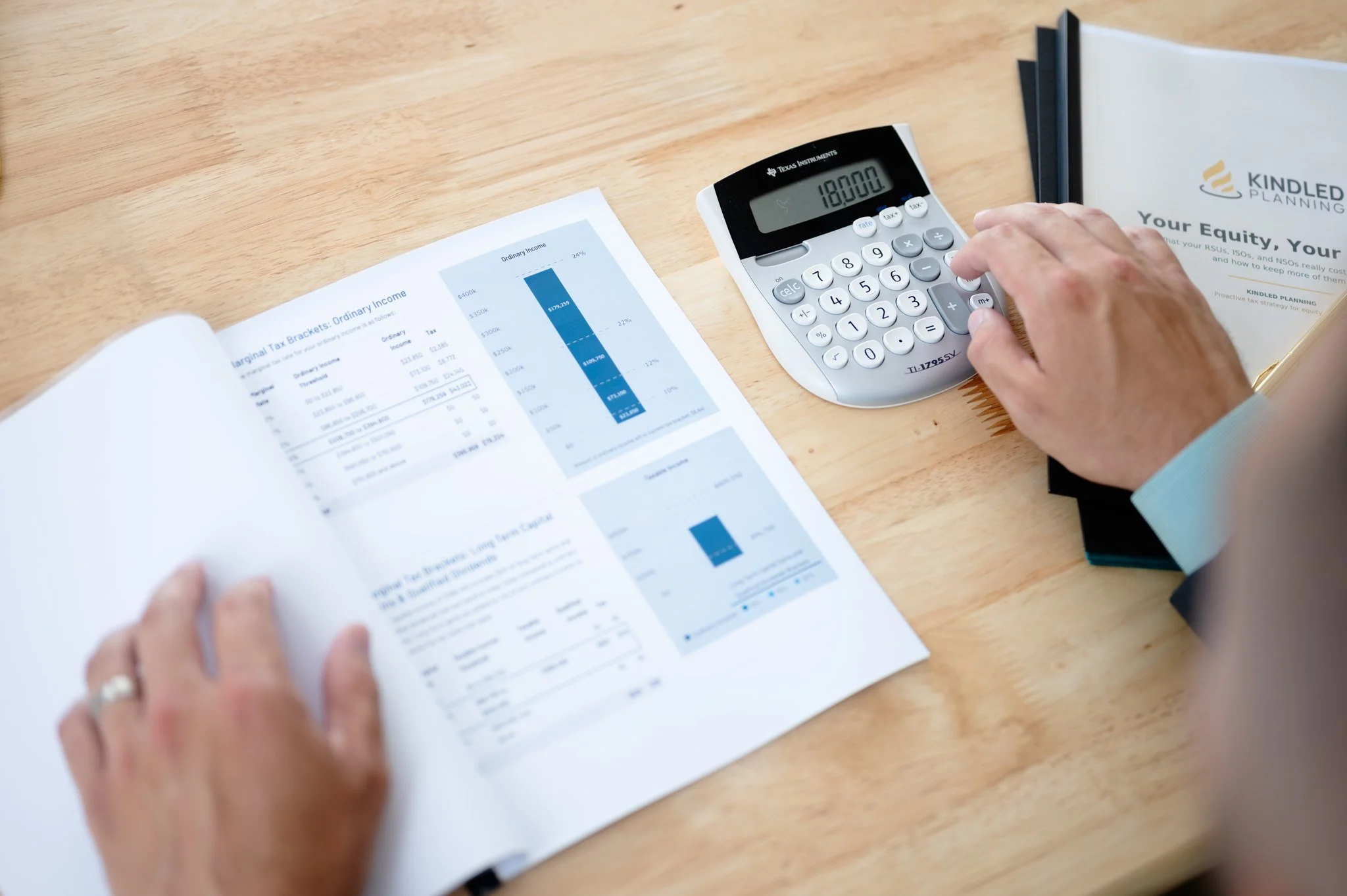 A person using a calculator on a wooden desk with financial documents and a brochure related to equity and taxation.