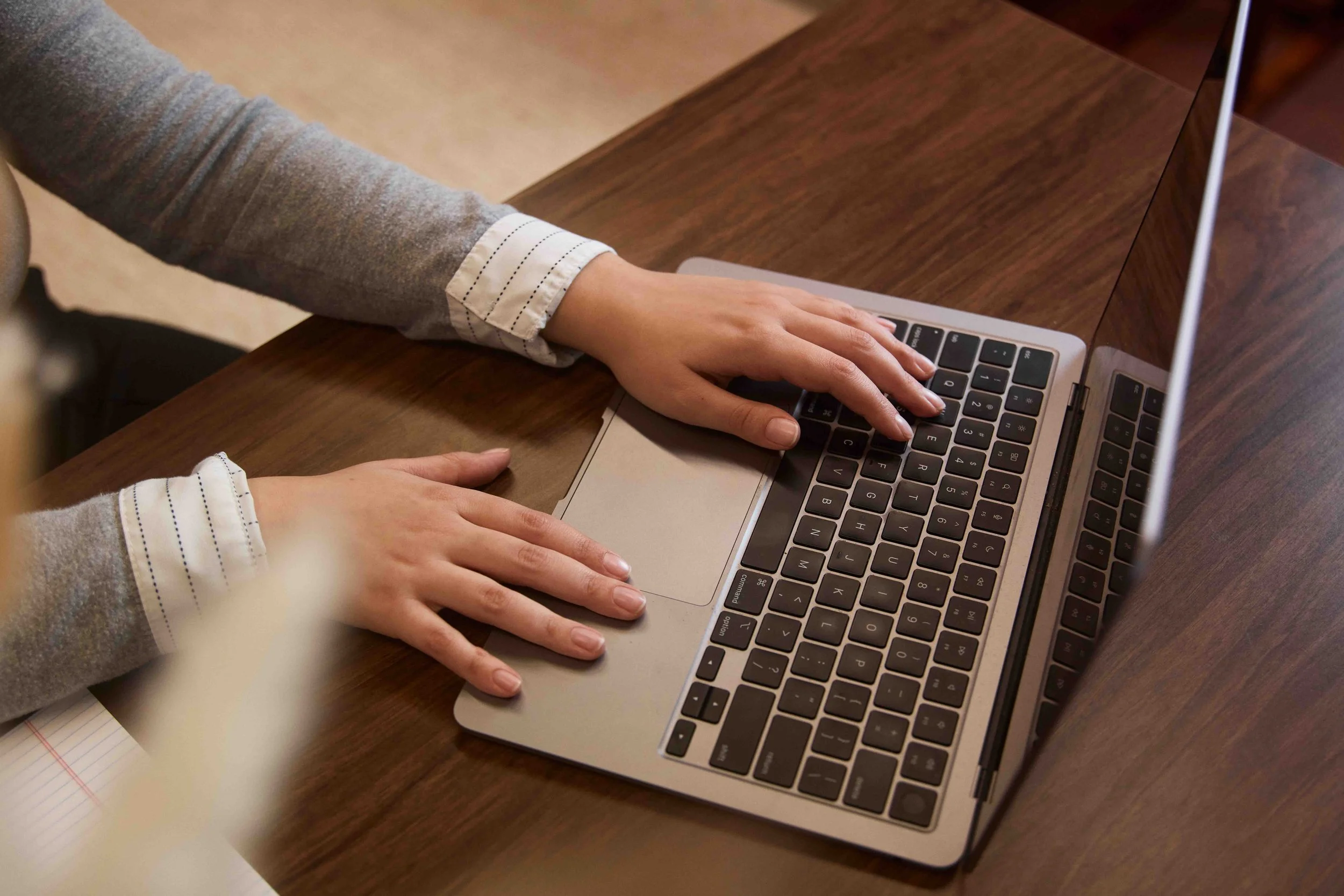 Person typing on a laptop keyboard placed on a wooden desk.