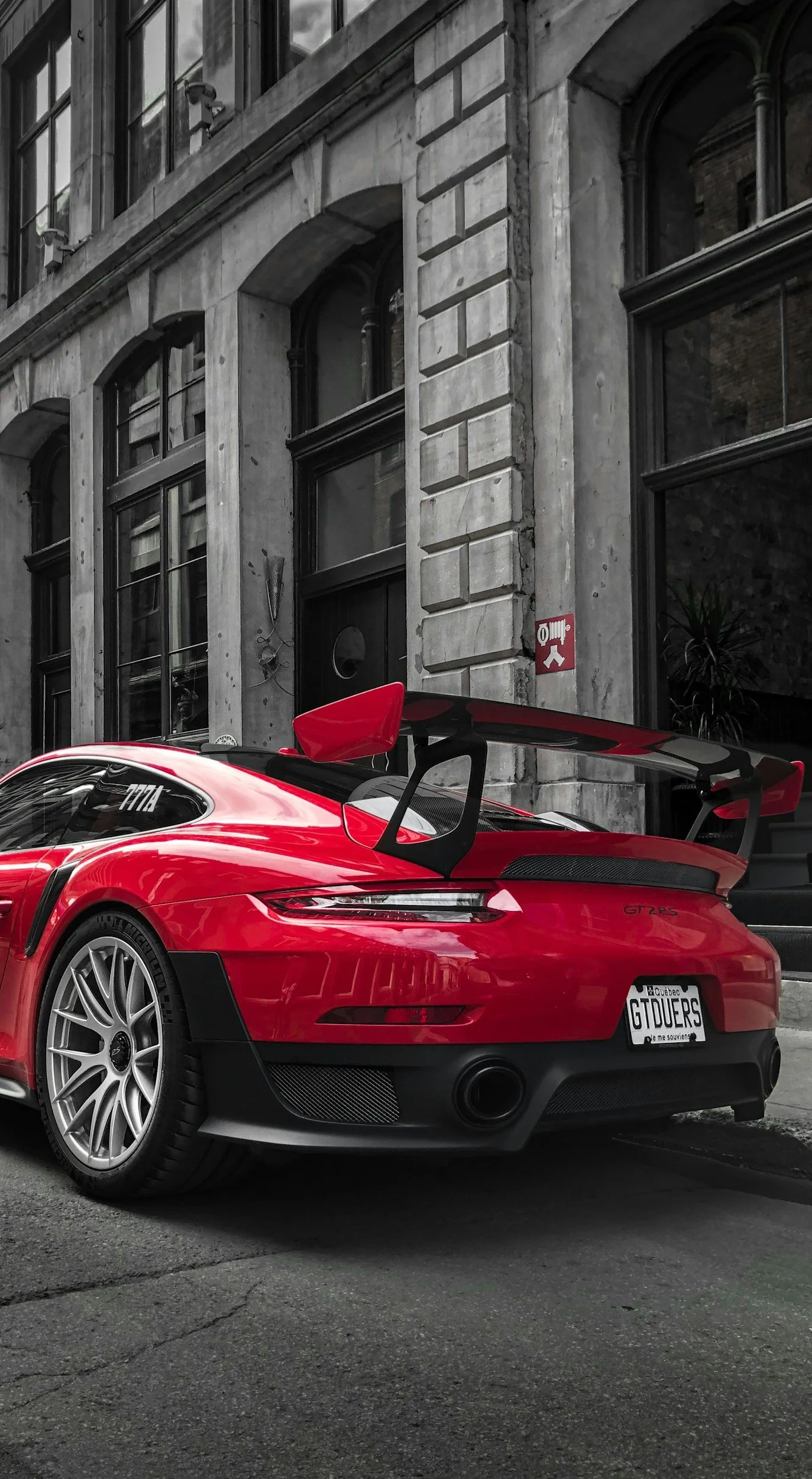 A red Porsche 911 GT2RS sports car parked on a city street, with an industrial-style building in the background.