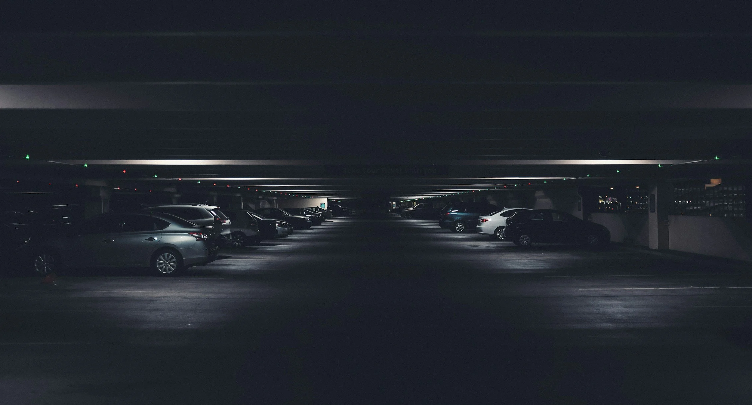 Underground parking garage with parked cars and overhead lighting.