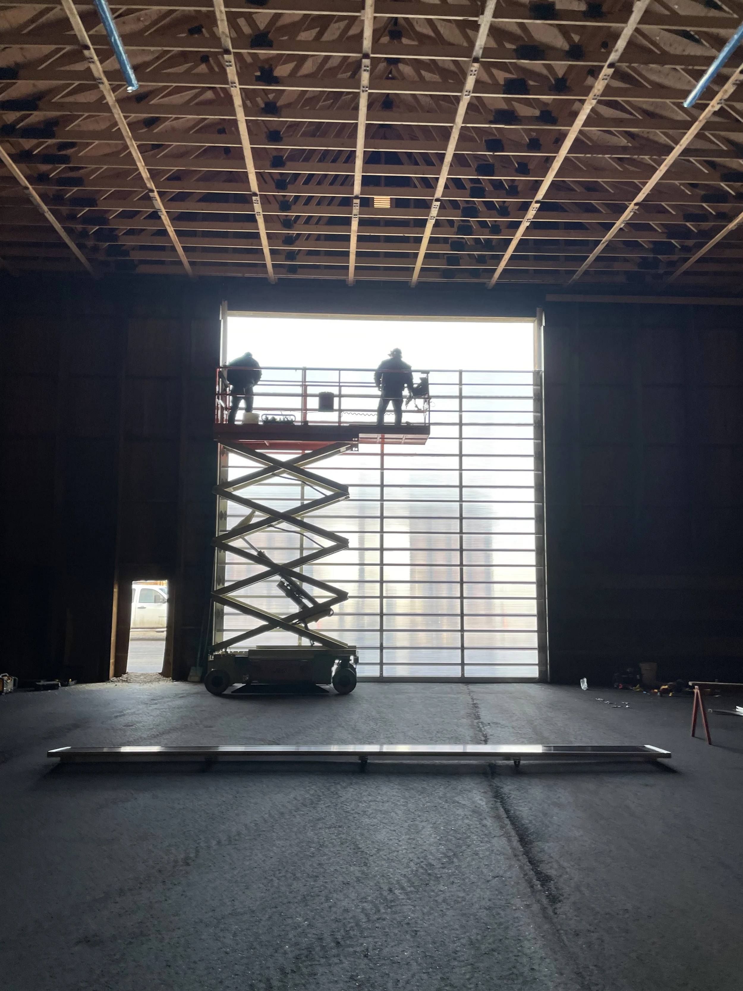 Workers on a scissor lift inside a warehouse constructing a large wall or door with a metal frame.