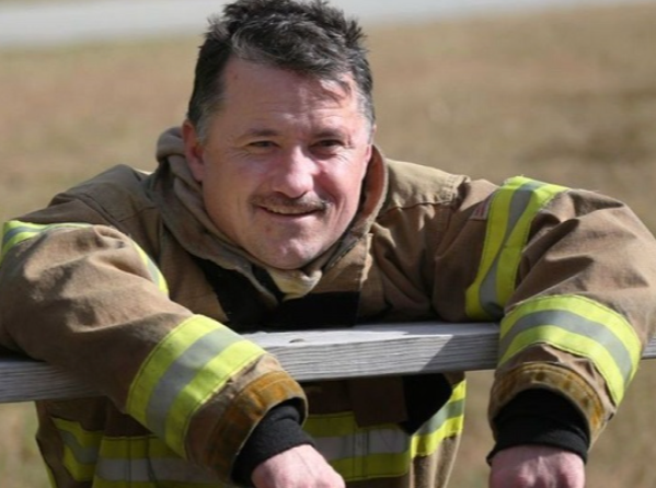 Firefighter in uniform resting his arms on a railing outdoors.