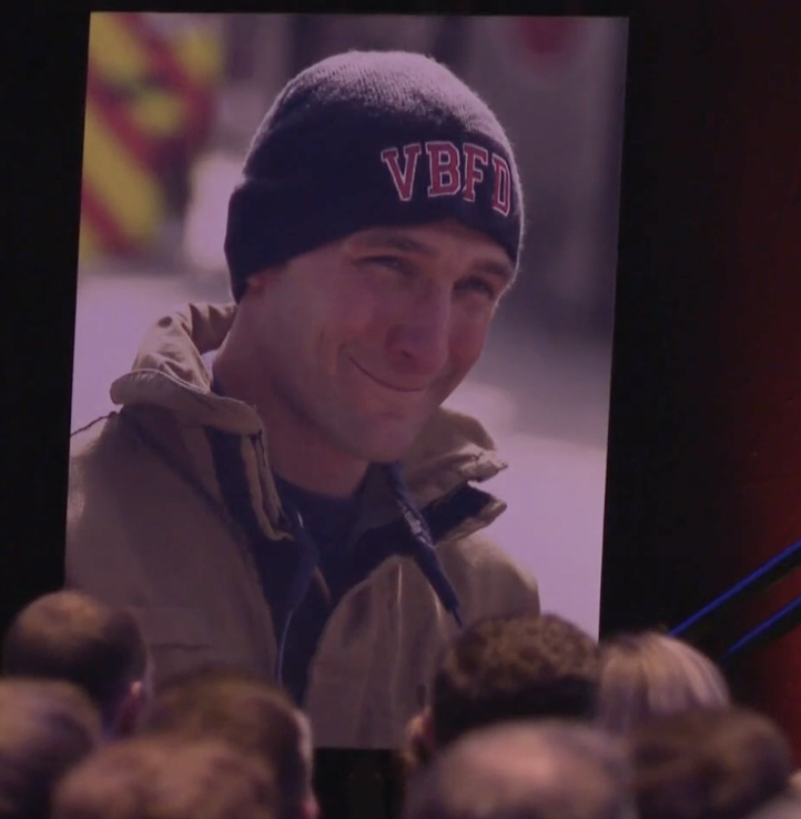 A man wearing a dark beanie with red embroidered initials 'VBFD' and a tan jacket.