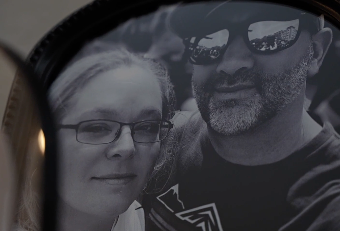 Black and white photograph of a smiling woman with glasses and a man with a beard wearing sunglasses.