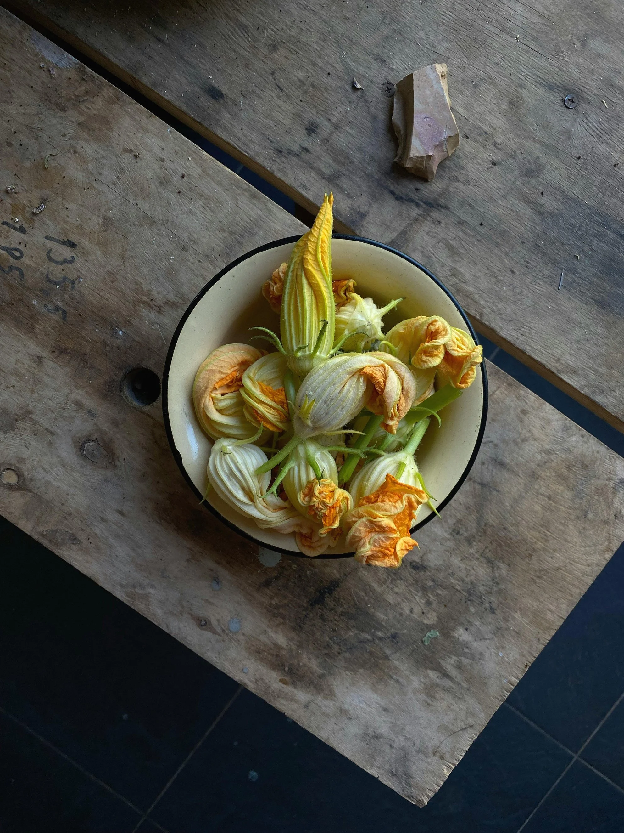 A bowl of zucchini blossoms on a rustic wooden table.