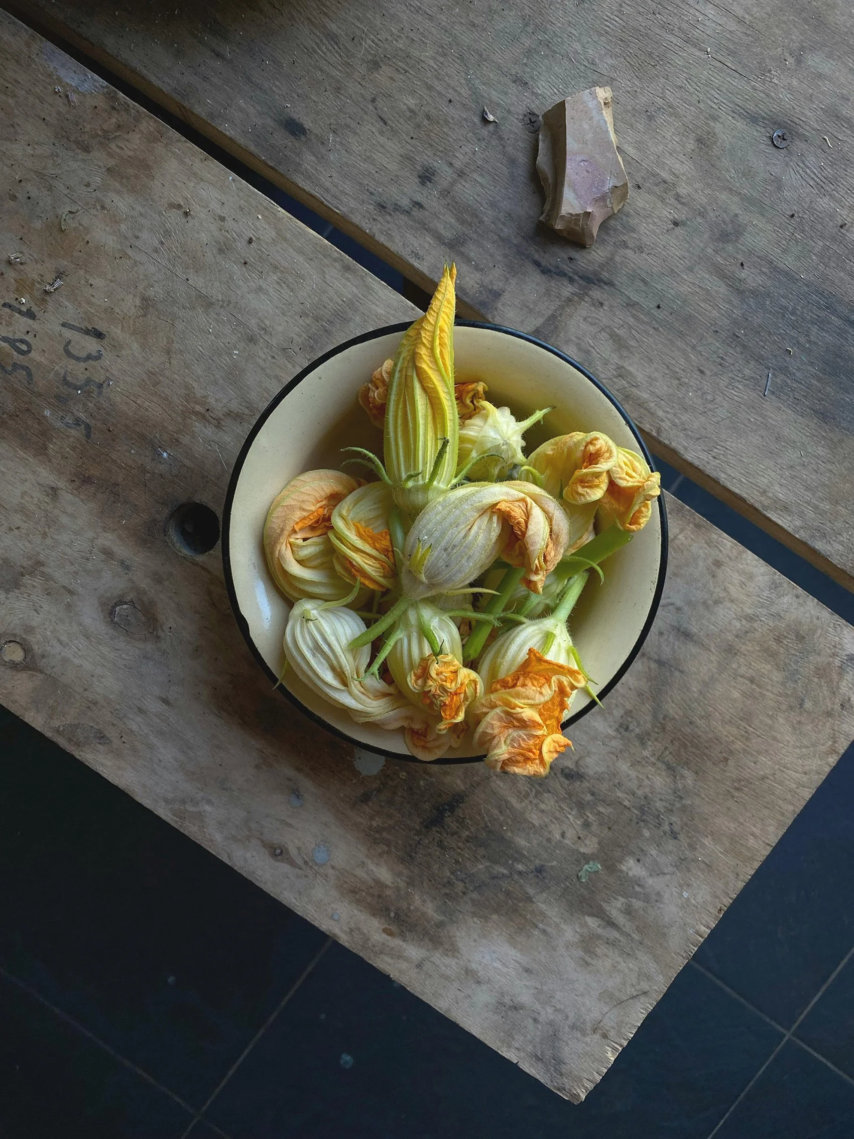 A bowl containing wilted yellow and white squash blossoms on a rustic wooden table.