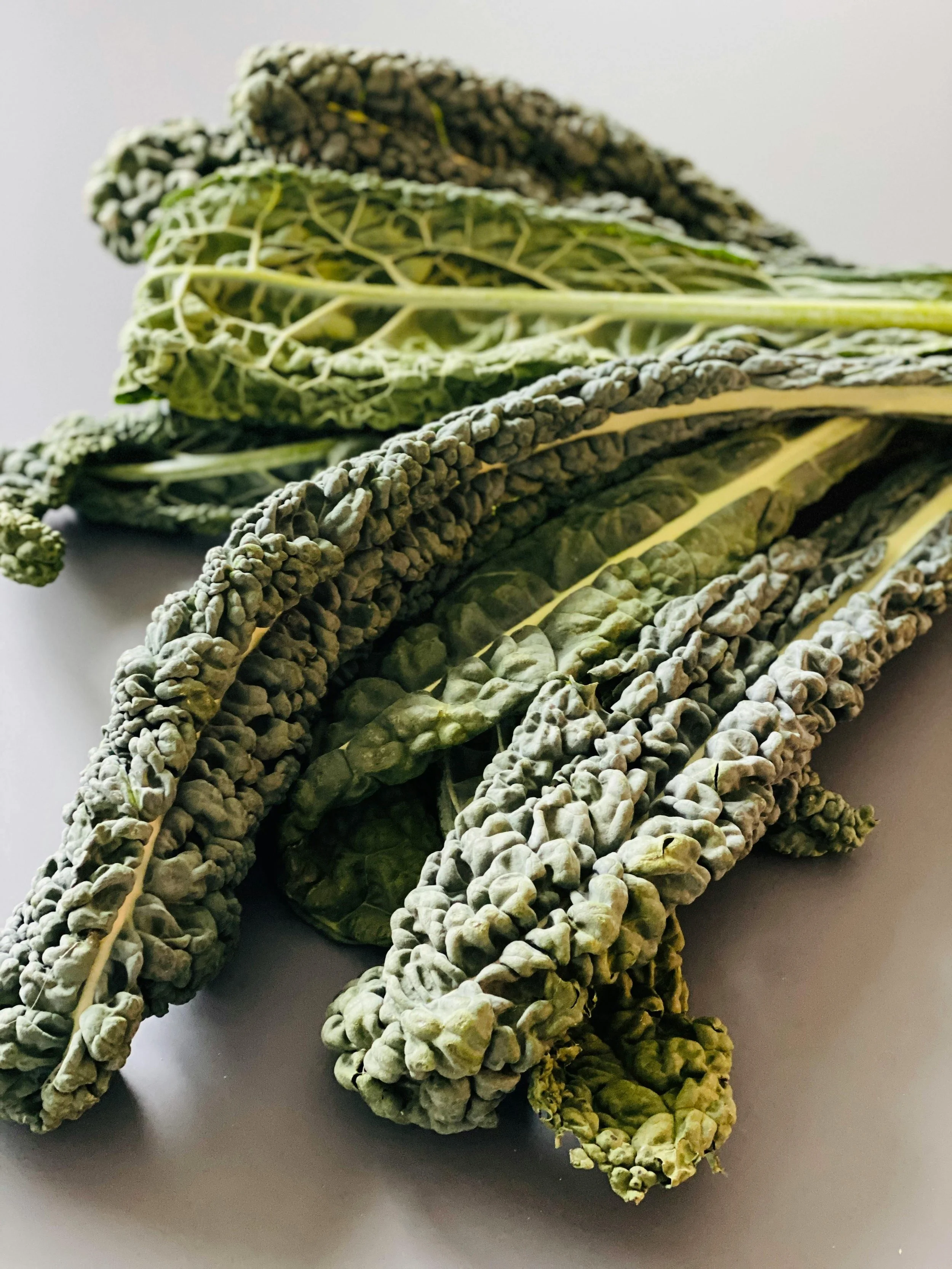 Close-up of fresh kale leaves with curly edges and visible veins, some leaves folded and overlapping, on a white surface.