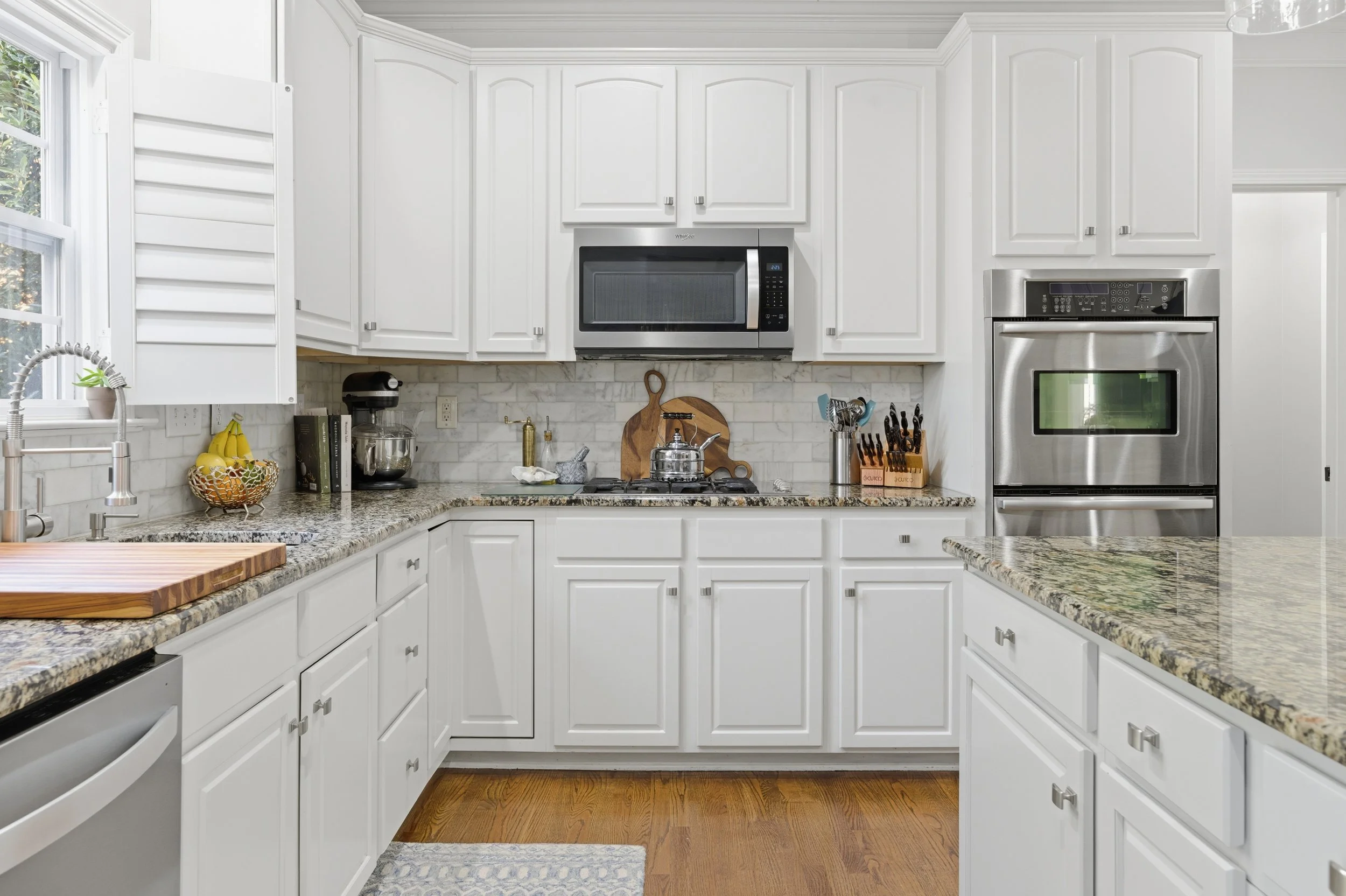 Modern kitchen with white cabinets, granite countertops, stainless steel appliances, and hardwood floors.