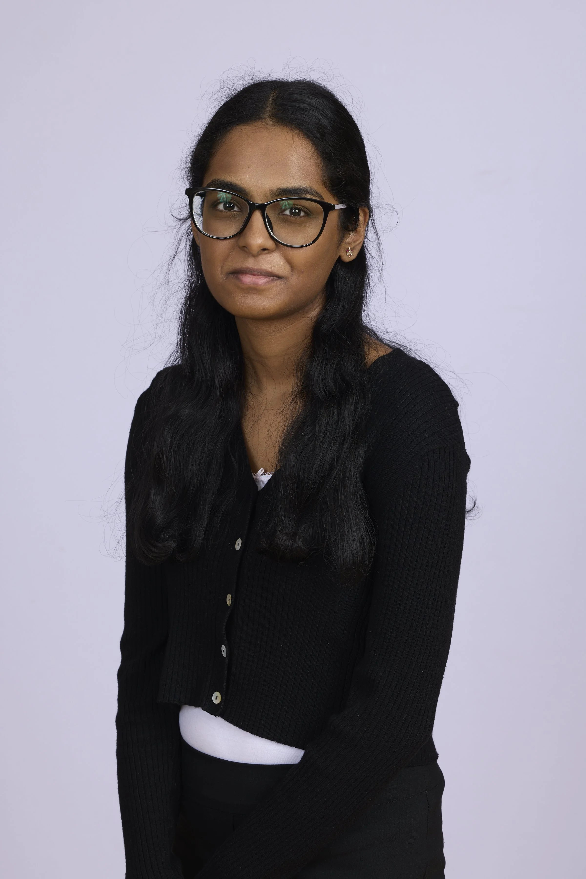 A young woman with black hair, glasses, and a black cardigan, standing against a plain light background.