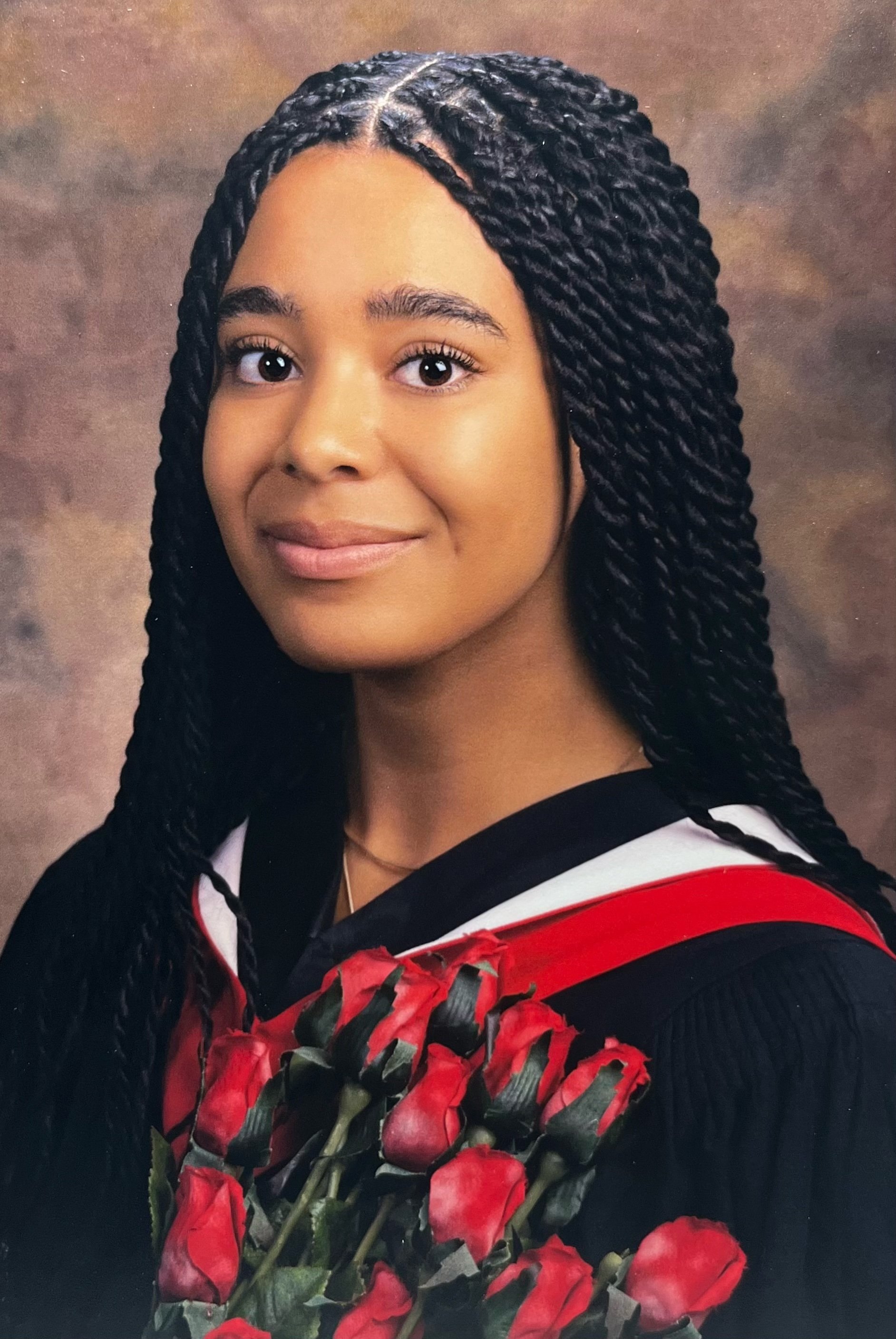 Young woman in graduation gown holding a bouquet of red roses