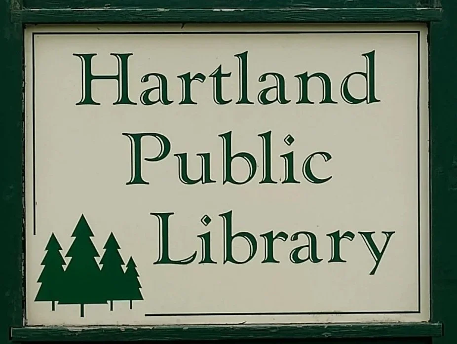 Sign for Hartland Public Library with green trees graphic.
