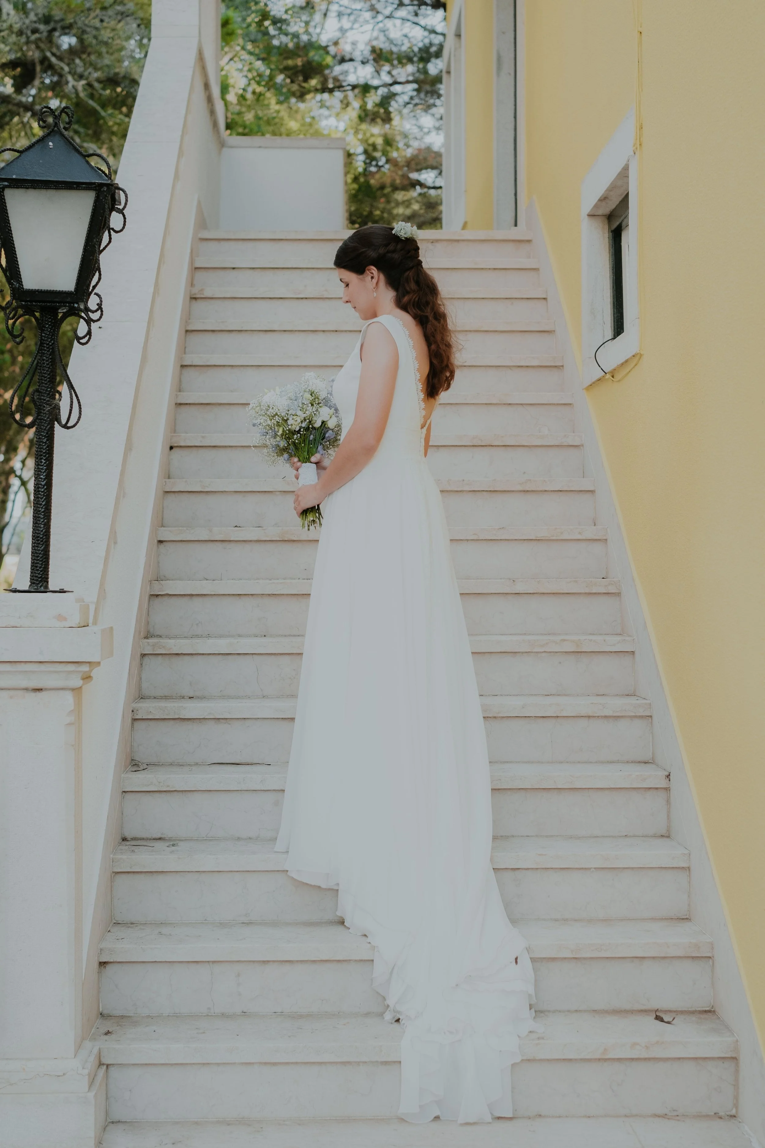 Bride standing on stairs holding a bouquet in an elegant editorial wedding portrait in Portugal