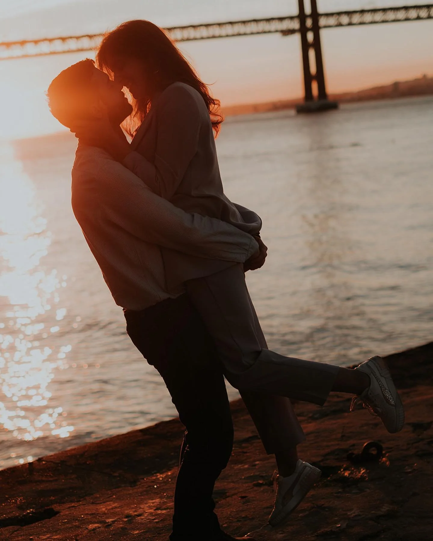 Couple embracing at sunset by the river with the 25 de Abril bridge in Lisbon