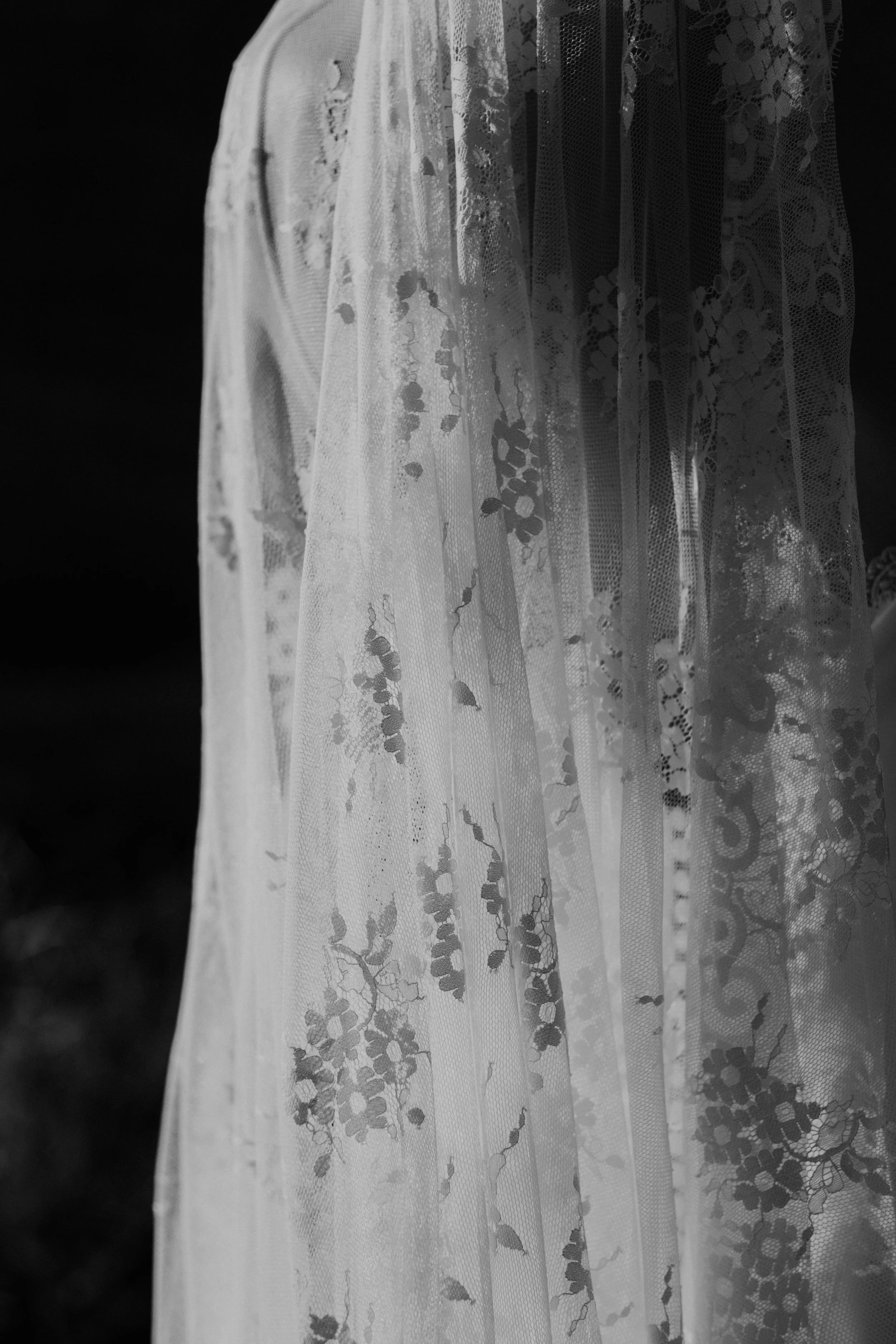 Close-up in black and white of a delicate floral lace bridal veil with soft natural lighting.