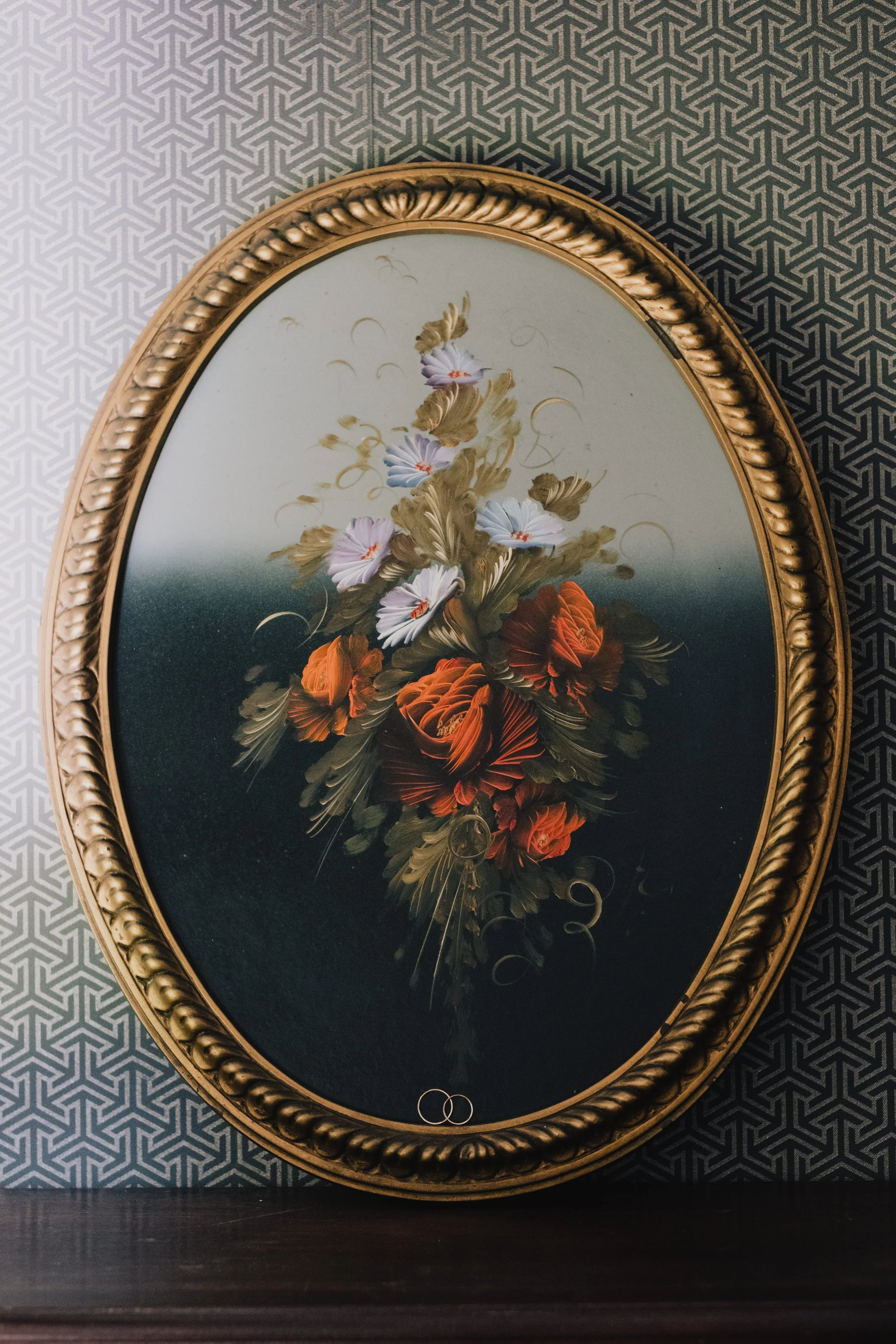 Vintage floral painting in an ornate gold oval frame against geometric wallpaper, captured in soft natural light by Carlos Mendes Photography.