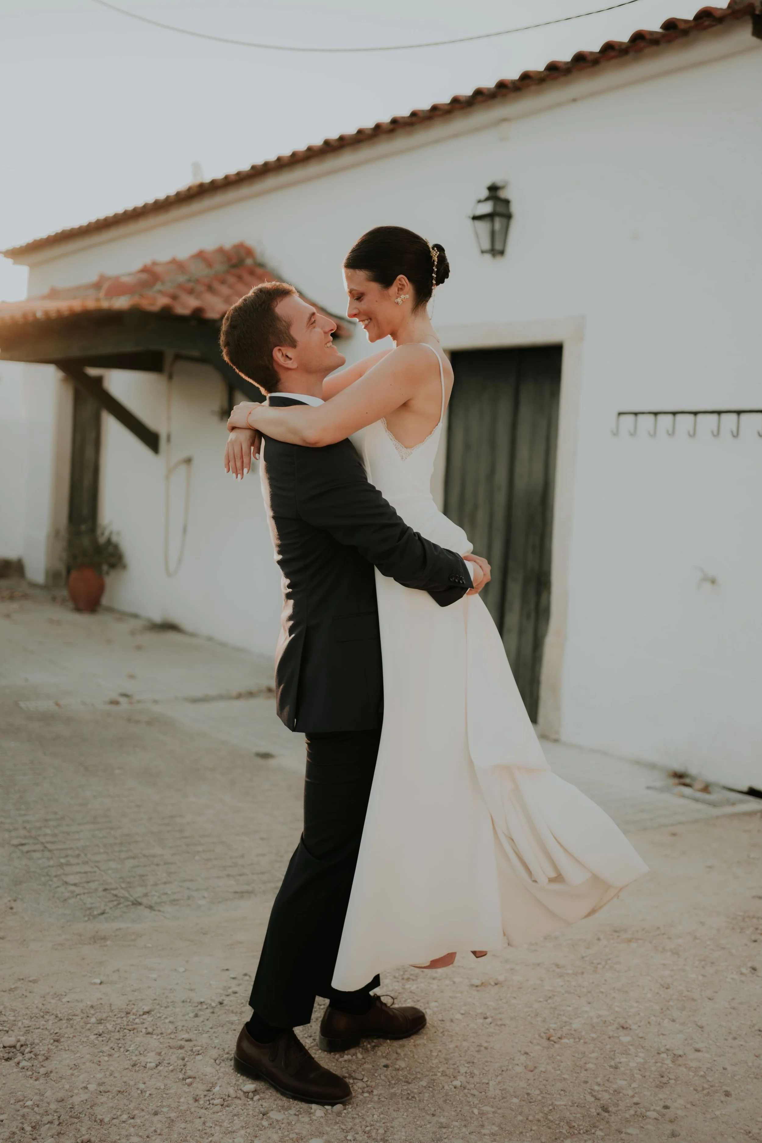 Groom lifting his smiling bride in a romantic moment during golden hour in a rustic courtyard.