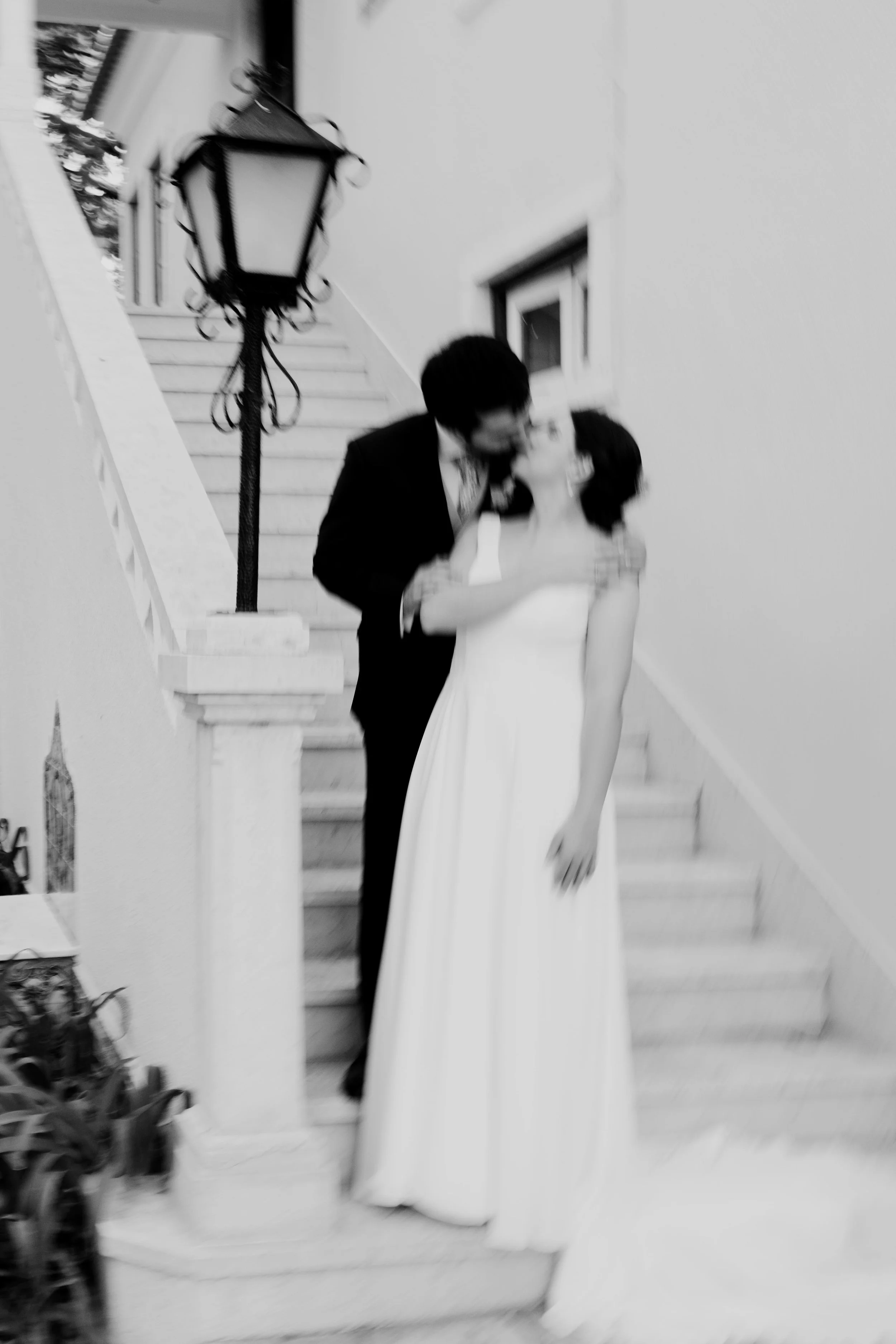 Black and white blurred photo of a bride and groom embracing on a stone staircase, evoking a sense of motion and intimacy, captured by Carlos Mendes Photography.