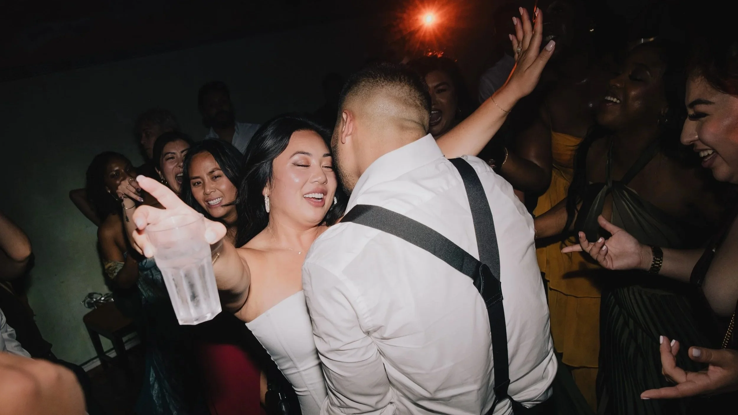 Energetic wedding reception scene with guests dancing closely together under warm, colorful lighting, capturing a joyful and vibrant party atmosphere.