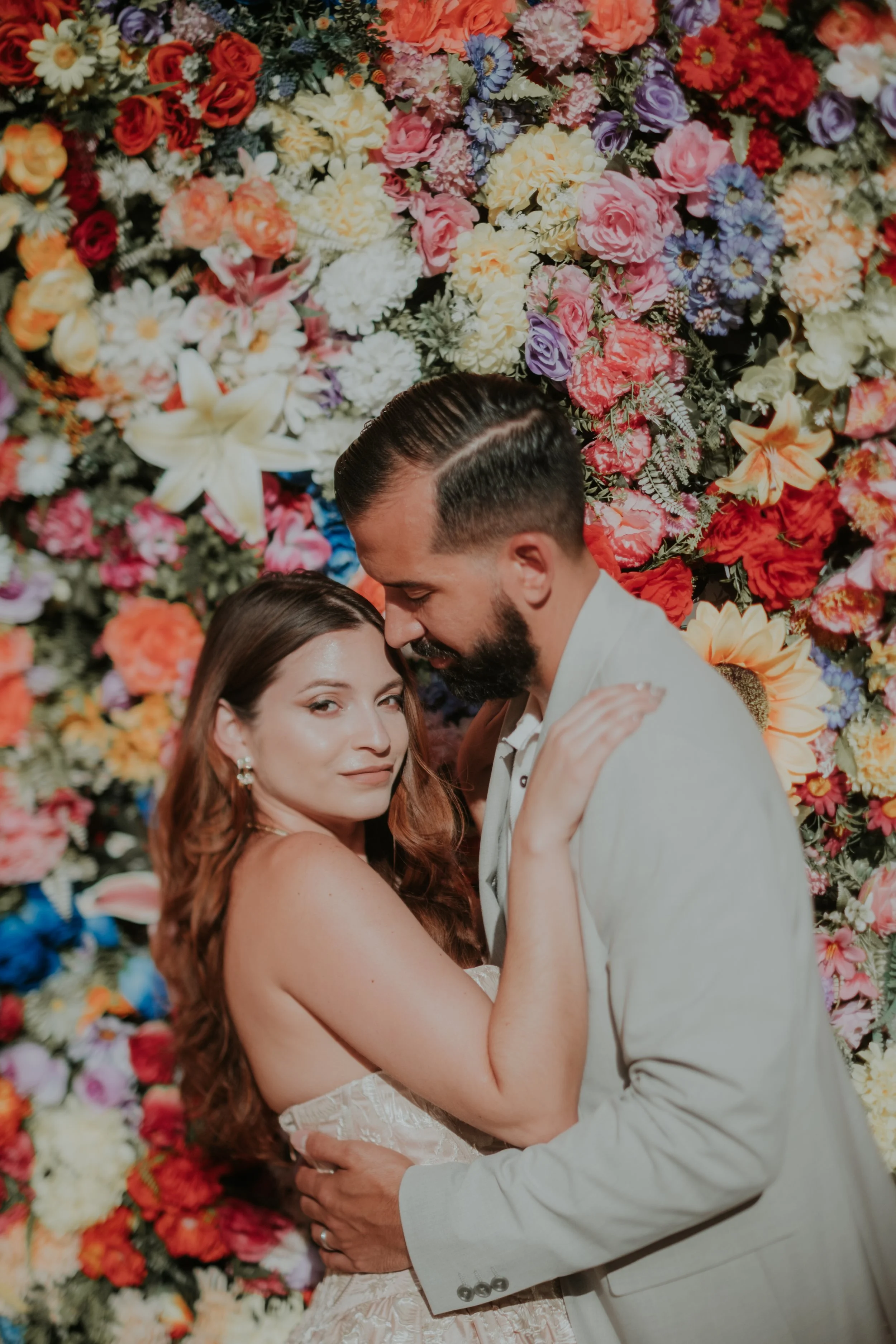 Bride and groom embracing in front of a floral background during an intimate elopement