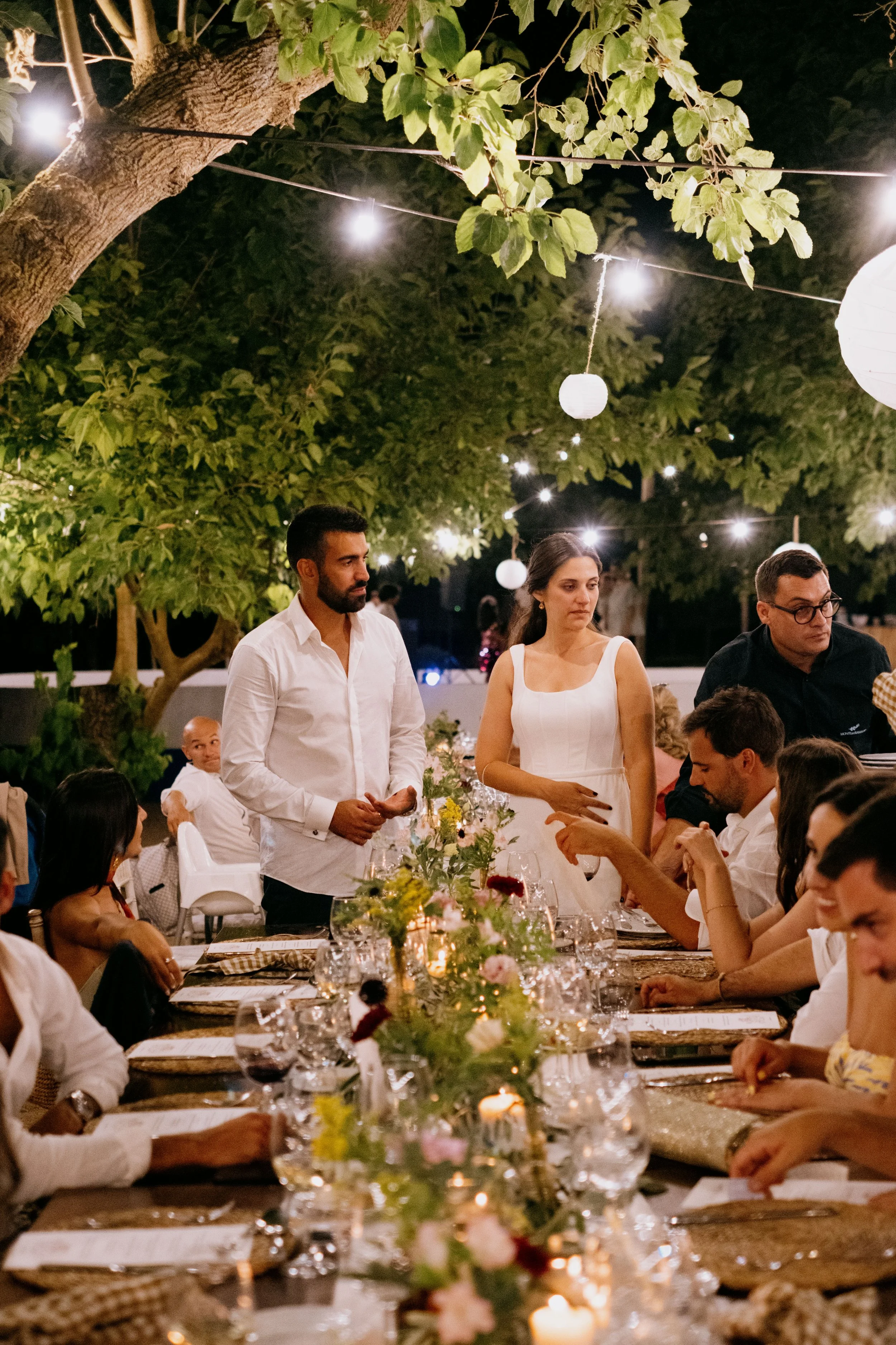 Outdoor wedding dinner under string lights with guests seated in a warm evening atmosphere