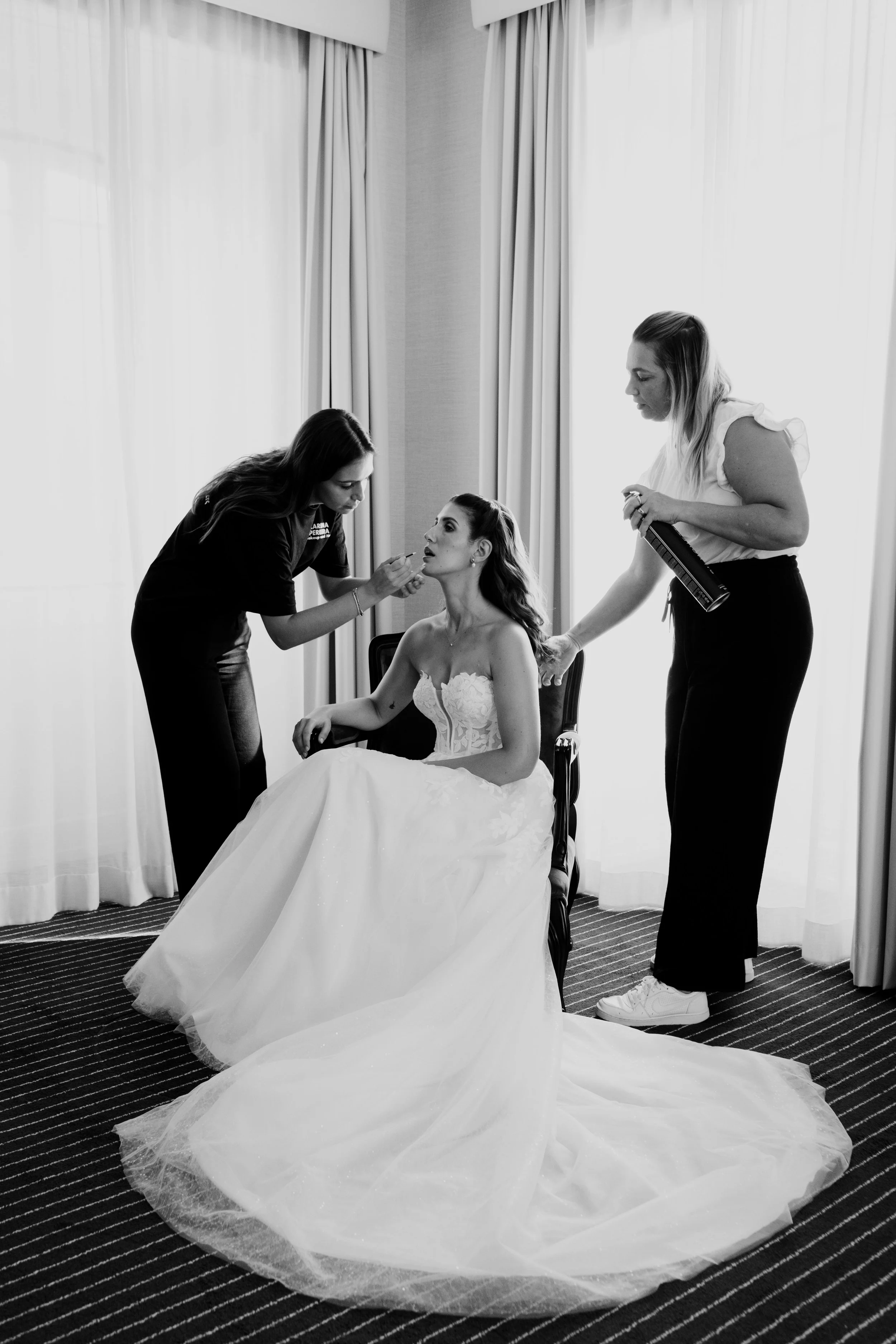 Bride getting ready with makeup artists during wedding preparations captured in black and white
